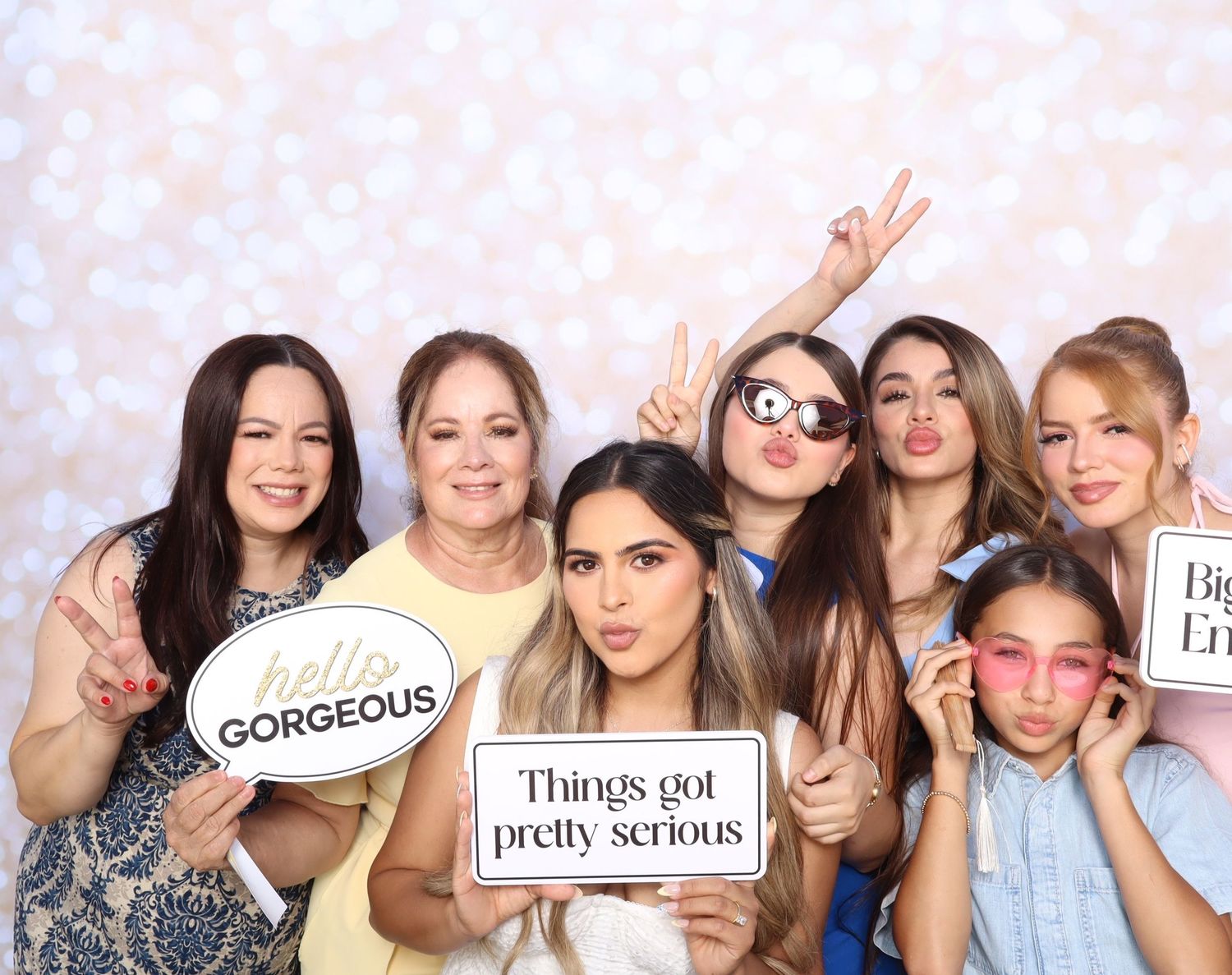 A group poses together with playful expressions and photo booth style props against a light background.