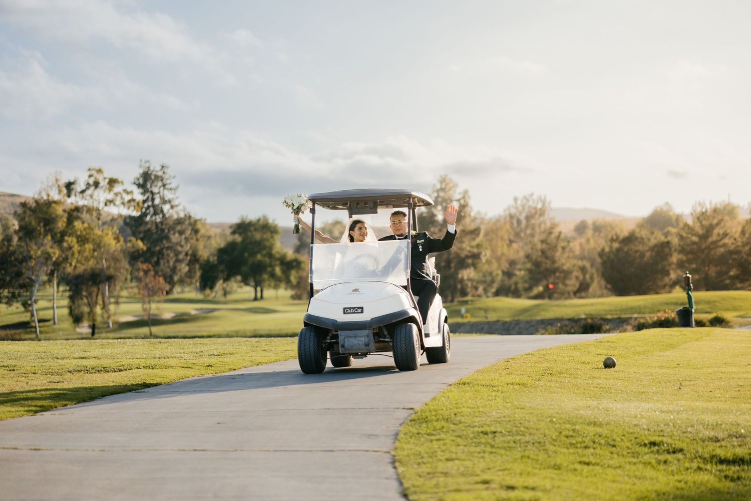 A golf cart drives along a sunny path on a green golf course.