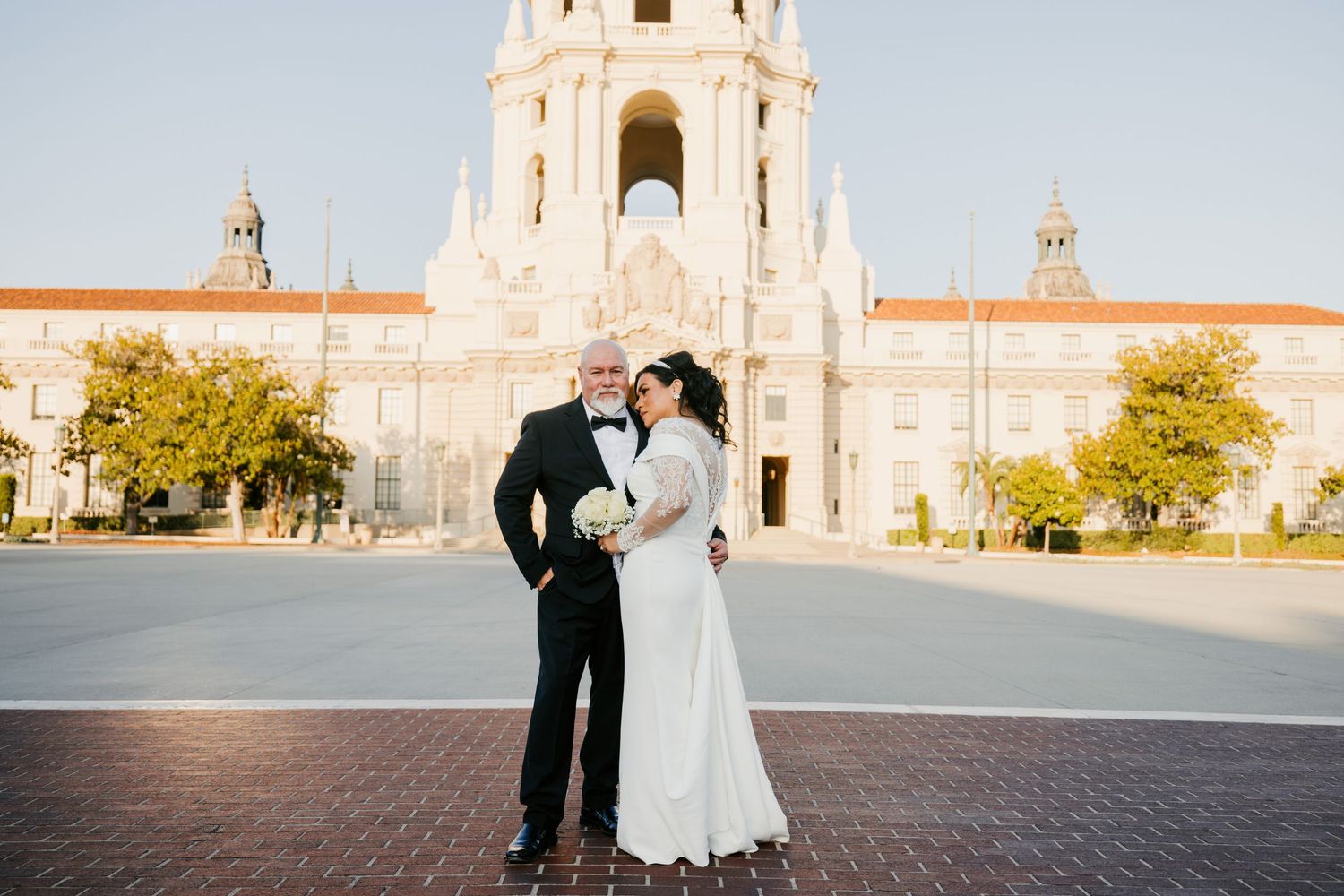 A couple poses in formal attire outside a grand Spanish colonial style building.