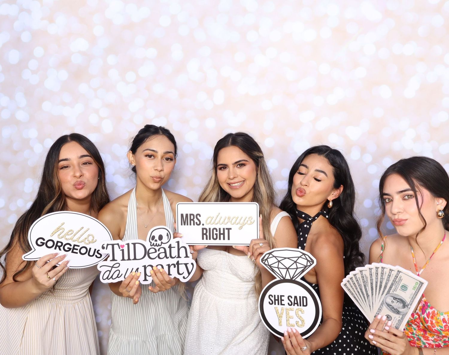 Five women pose in a bachelorette photo booth holding fun signs including Mrs. Always Right and She Said Yes.