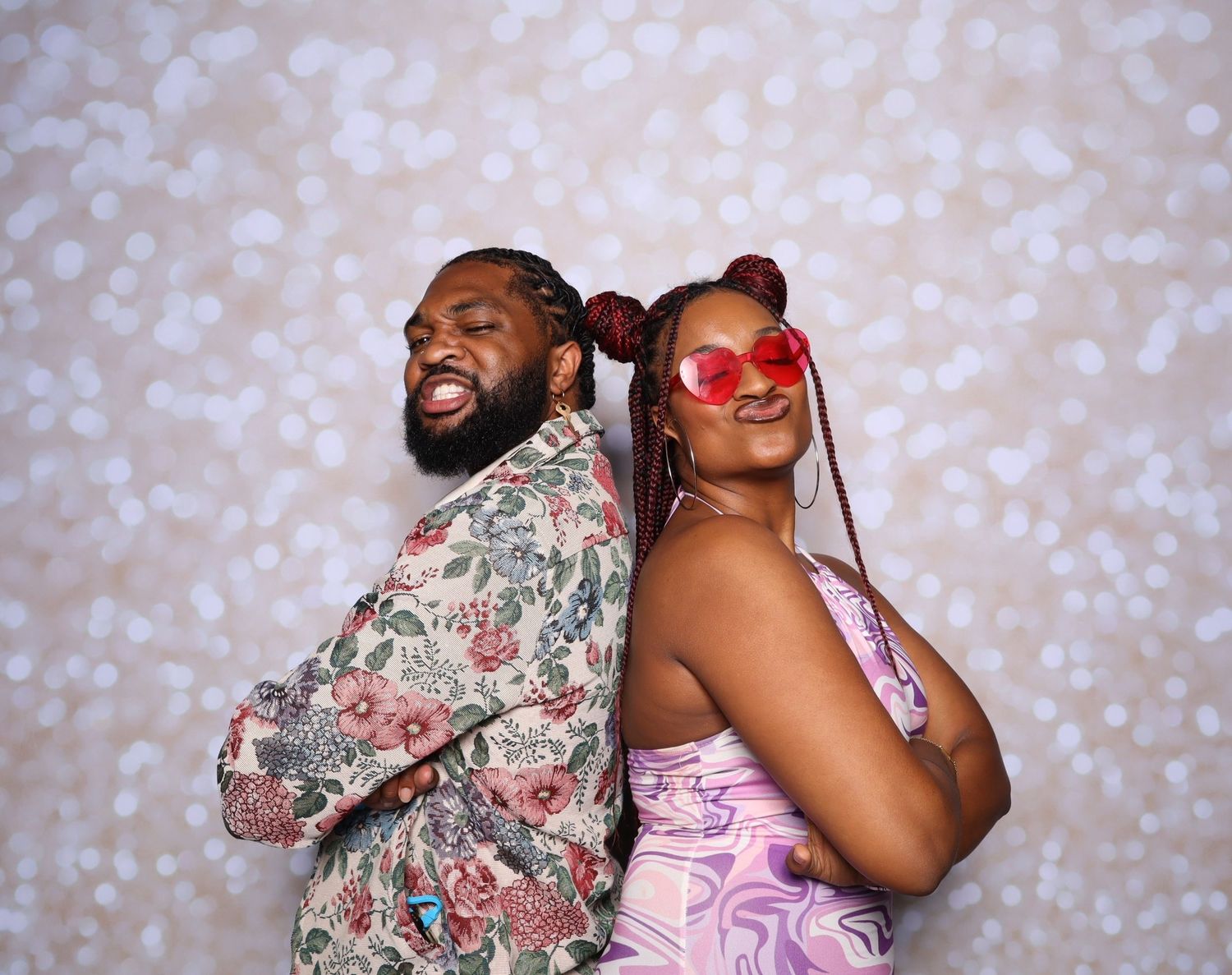 Two friends pose back-to-back smiling, wearing colorful outfits against a bokeh backdrop.