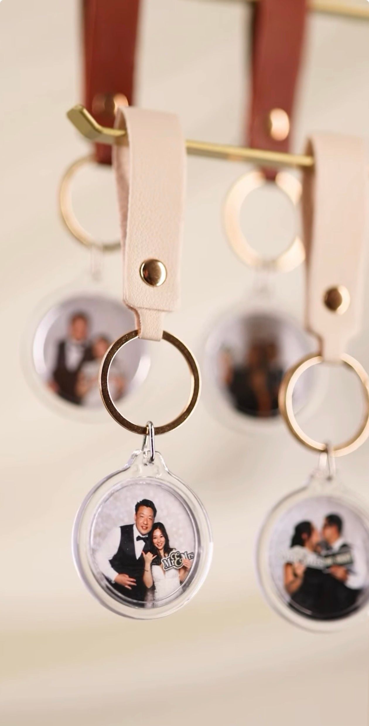 Clear acrylic photo keychains with pink leather straps hanging on a gold display bar showing wedding photos.