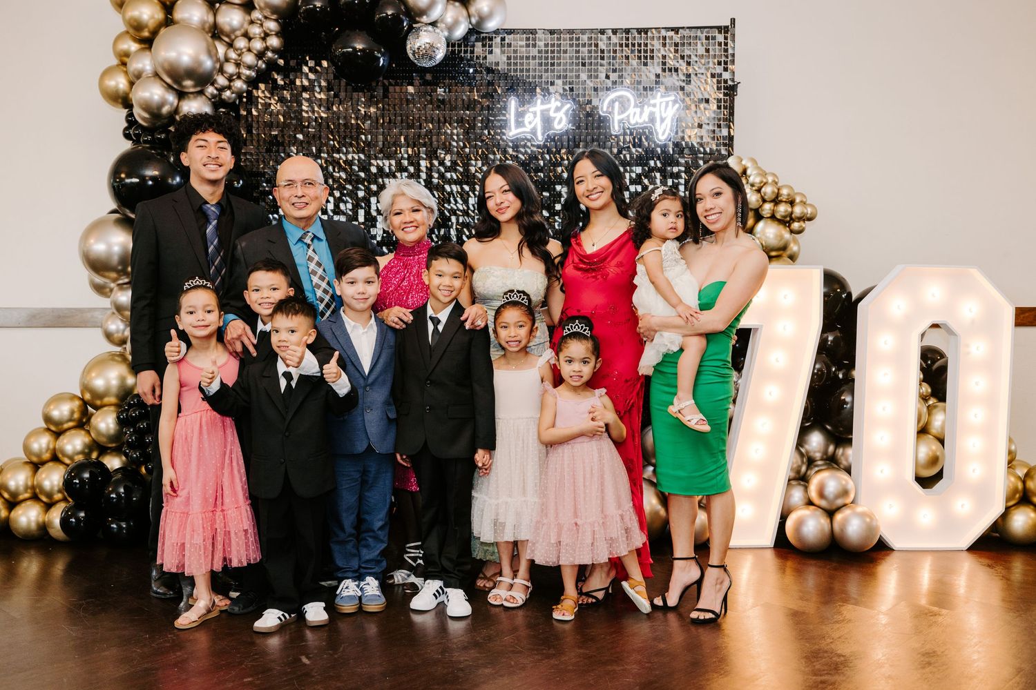 Formal group photo with gold and black balloon arch backdrop and illuminated numbers.