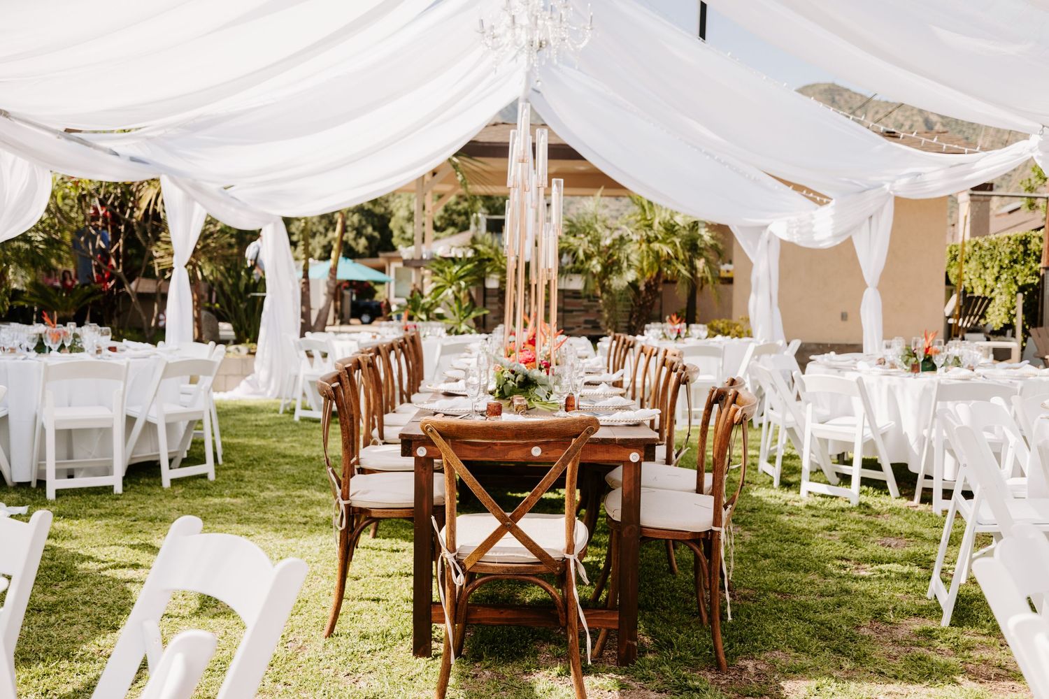 Wedding reception tent with rustic wooden tables and white chairs under flowing fabric.