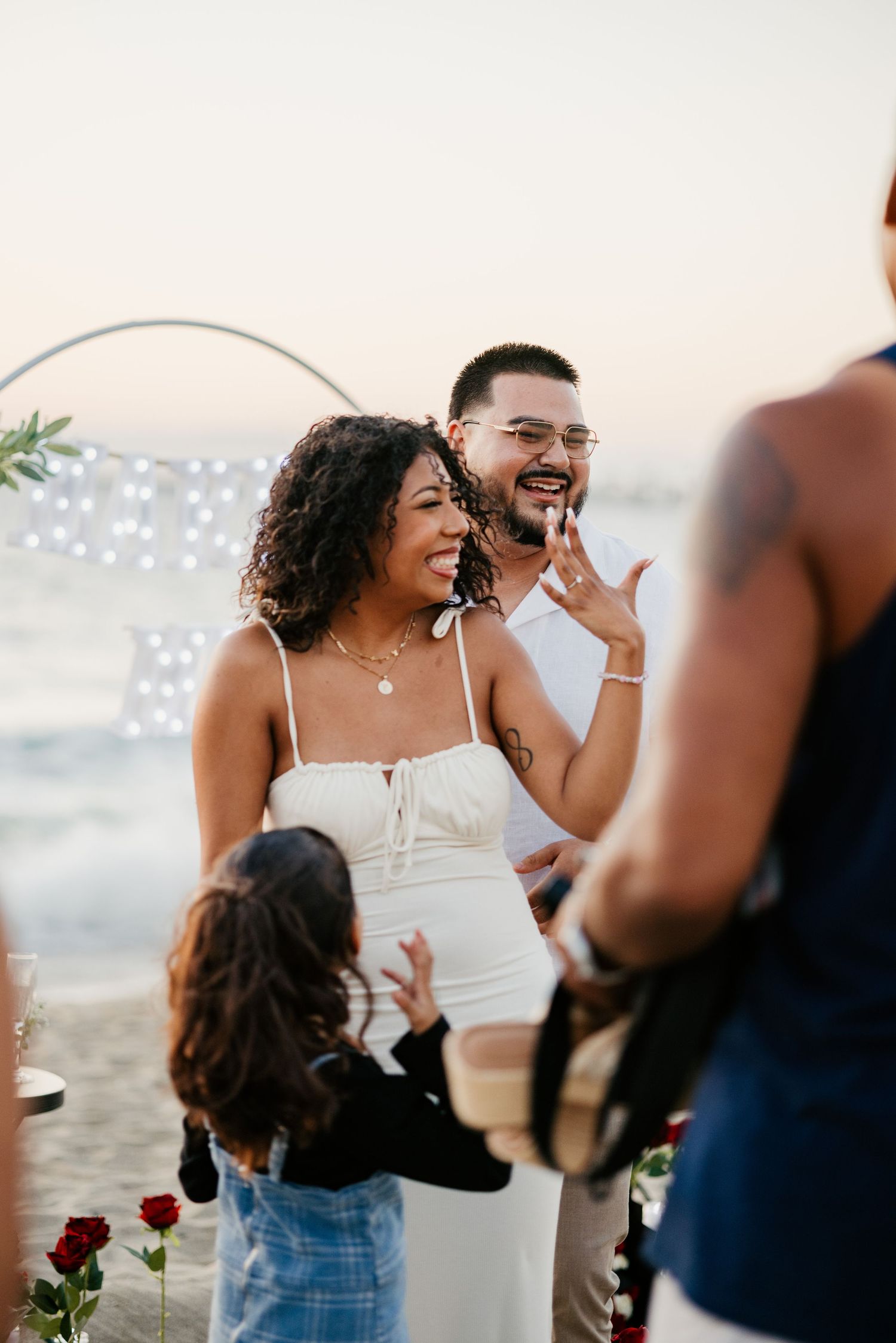 A candid moment of celebration during a beach proposal with decorative floral arrangements and lights.