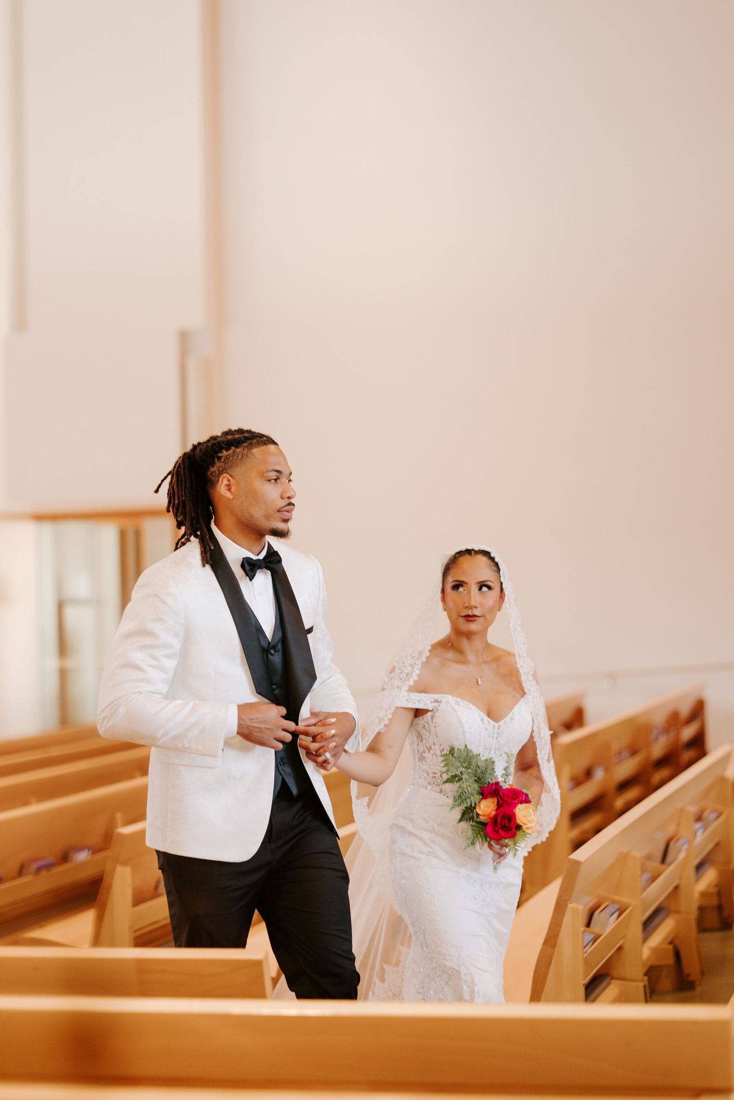 Elegant couple walks down church aisle during wedding ceremony with wooden pews.