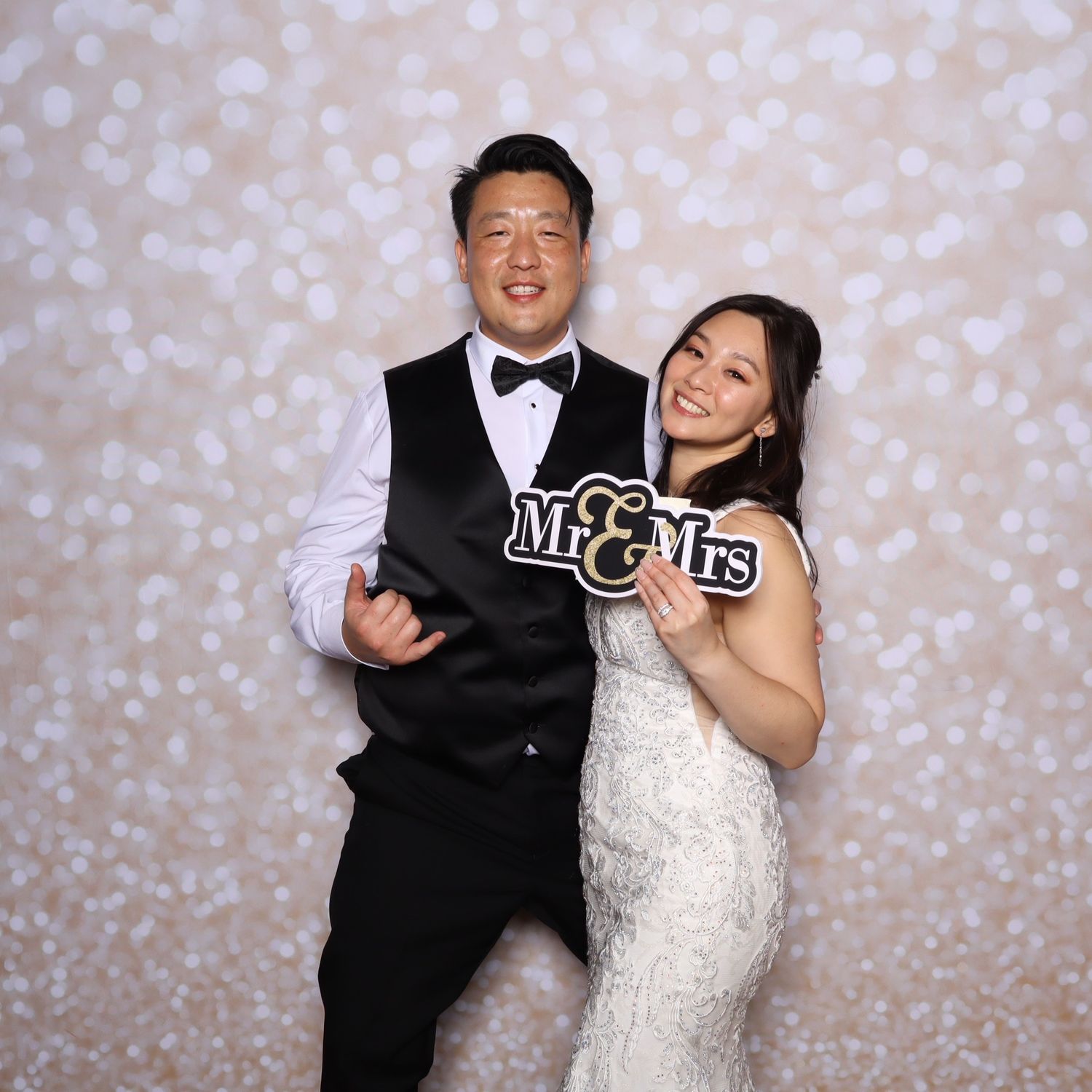 Newlywed couple posing with Mr. & Mrs. sign in front of bokeh backdrop at wedding photo booth.