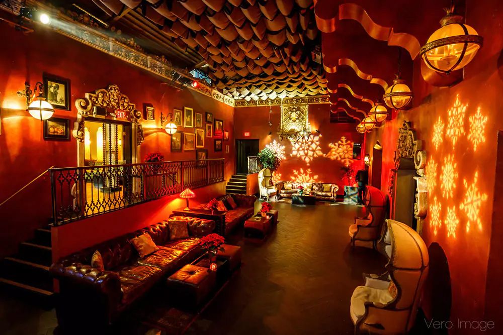 Cozy lounge interior with red walls, vintage lanterns, and plush seating under warm ambient lighting.