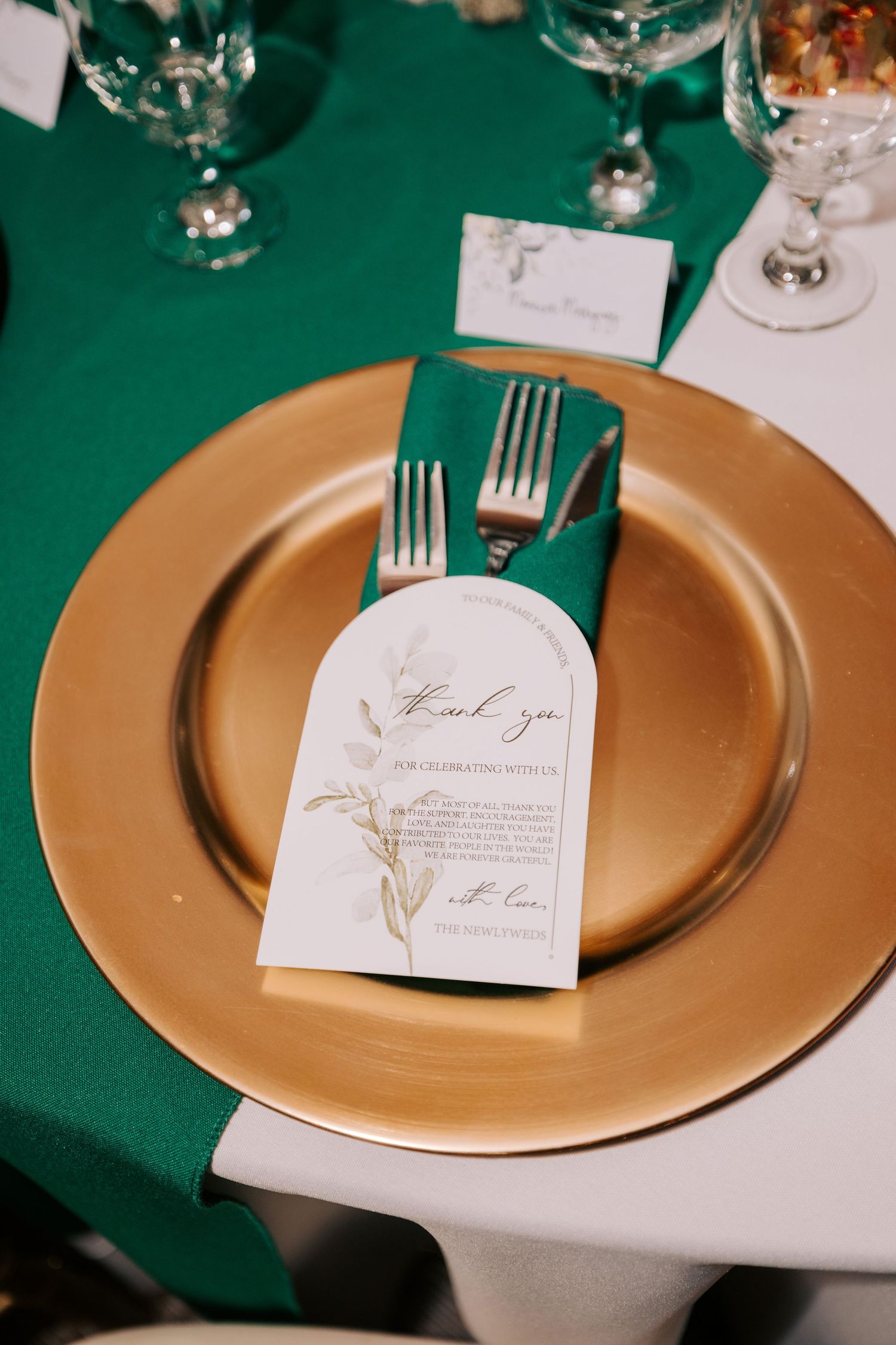 An elegant place setting with gold charger plate and green linens featuring a thank you card.