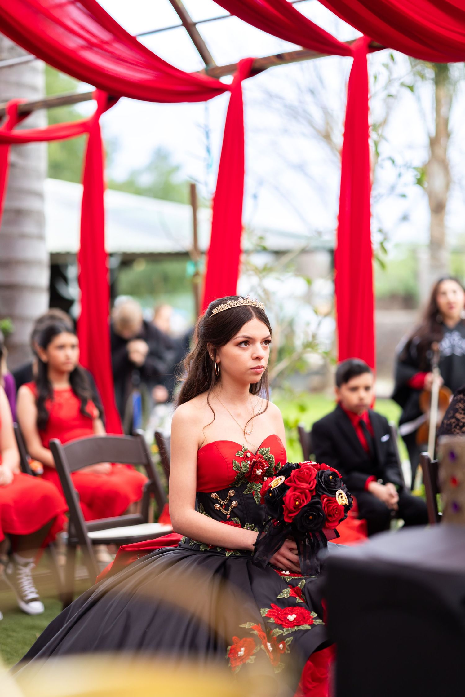 Elegant black and red ball gown with red roses bouquet under flowing red fabric decorations.