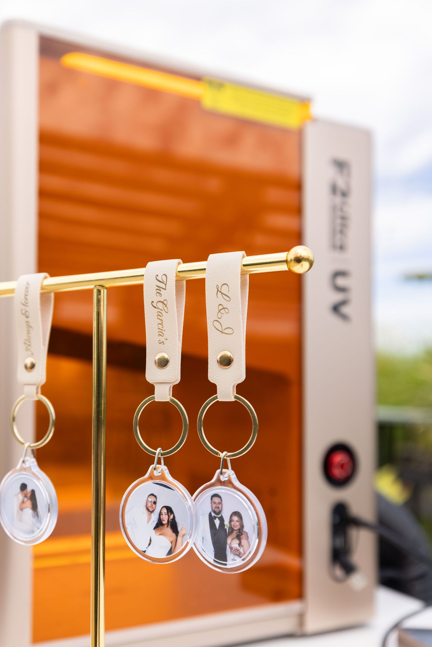 Custom wedding photo keychains with couple portraits hanging on a gold display rack near a UV printing machine.