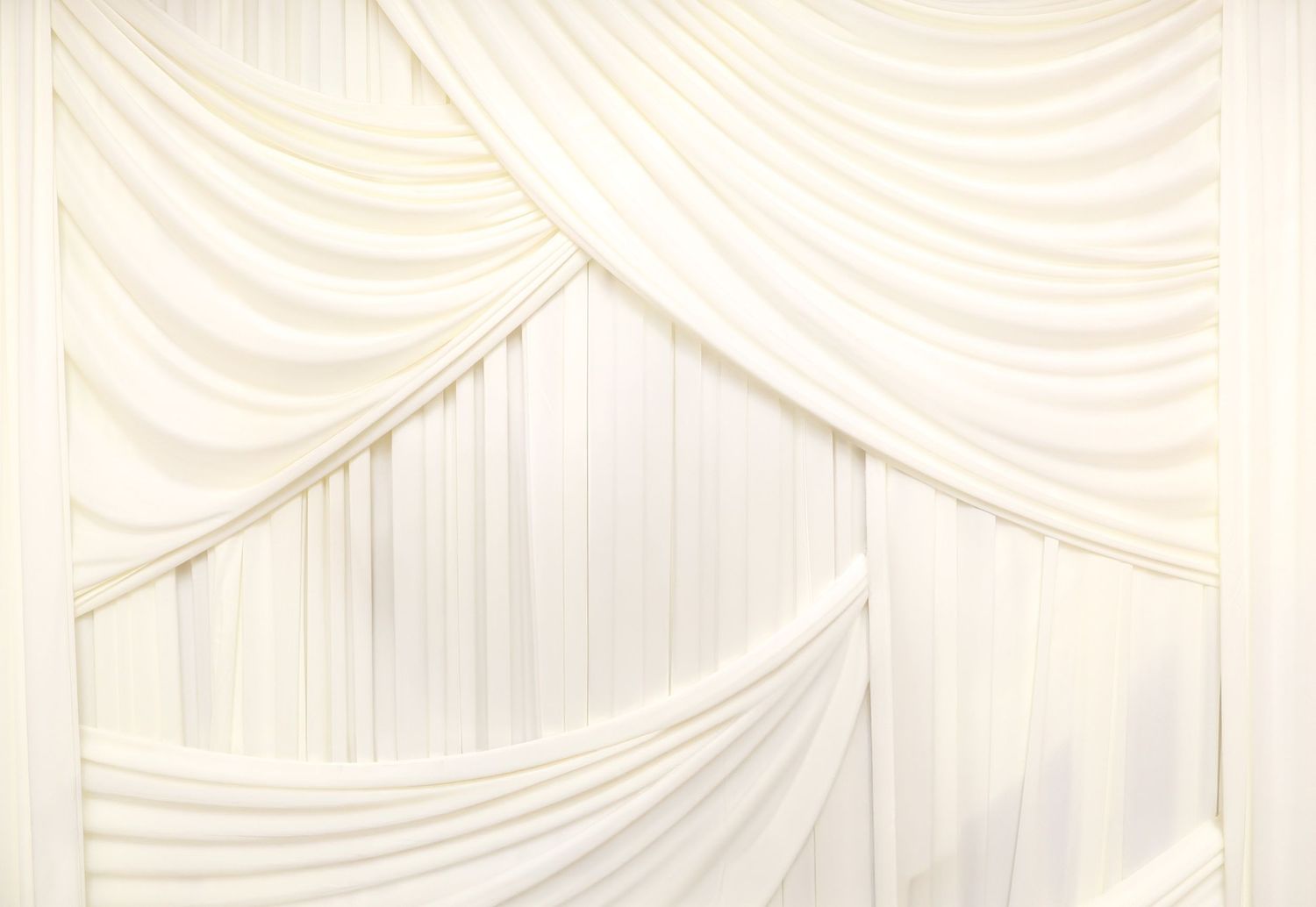 Elegant white draped fabric backdrop with soft folds and swags creates a romantic wedding or event setting.