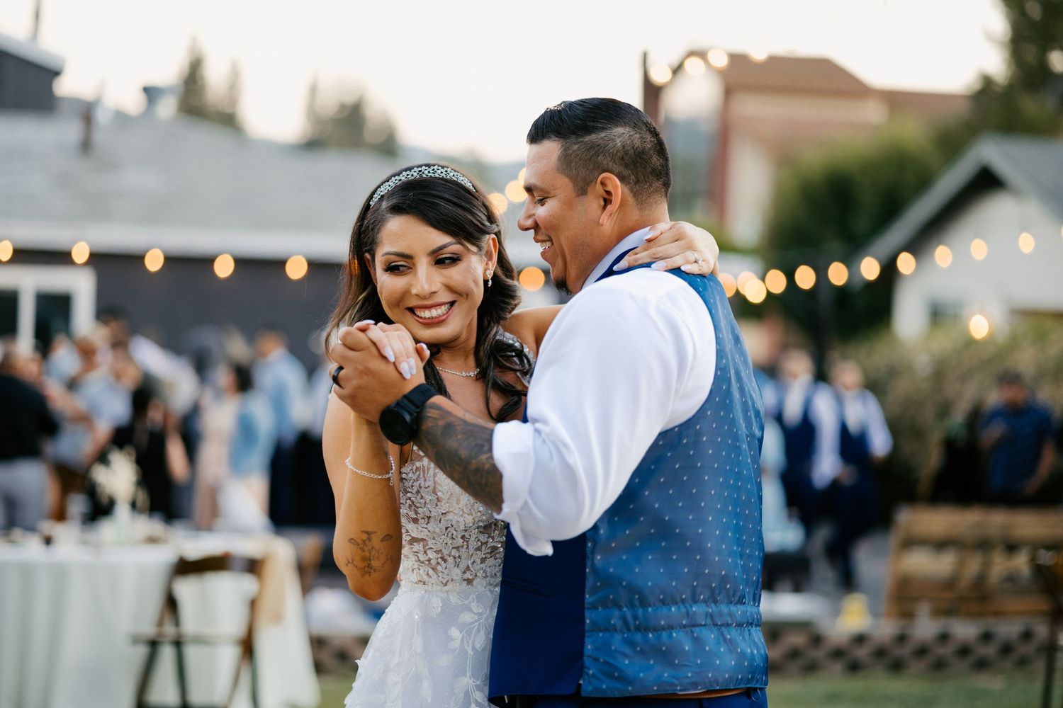 A couple dances joyfully at their outdoor wedding reception under twinkling lights.
