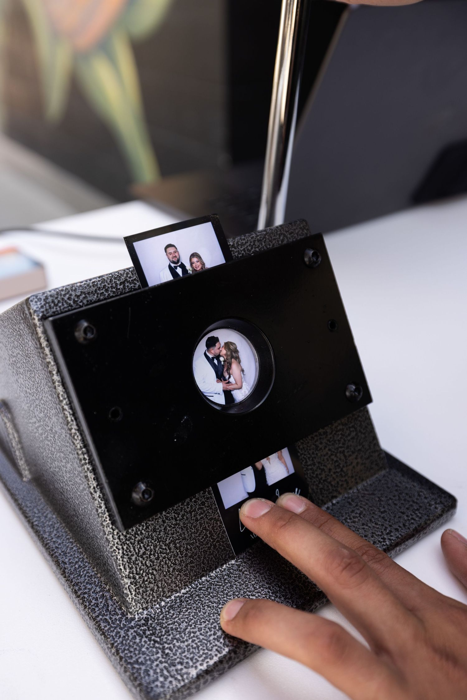 A hand operates a vintage photo slide viewer displaying wedding couple images on a textured gray machine on a white table.