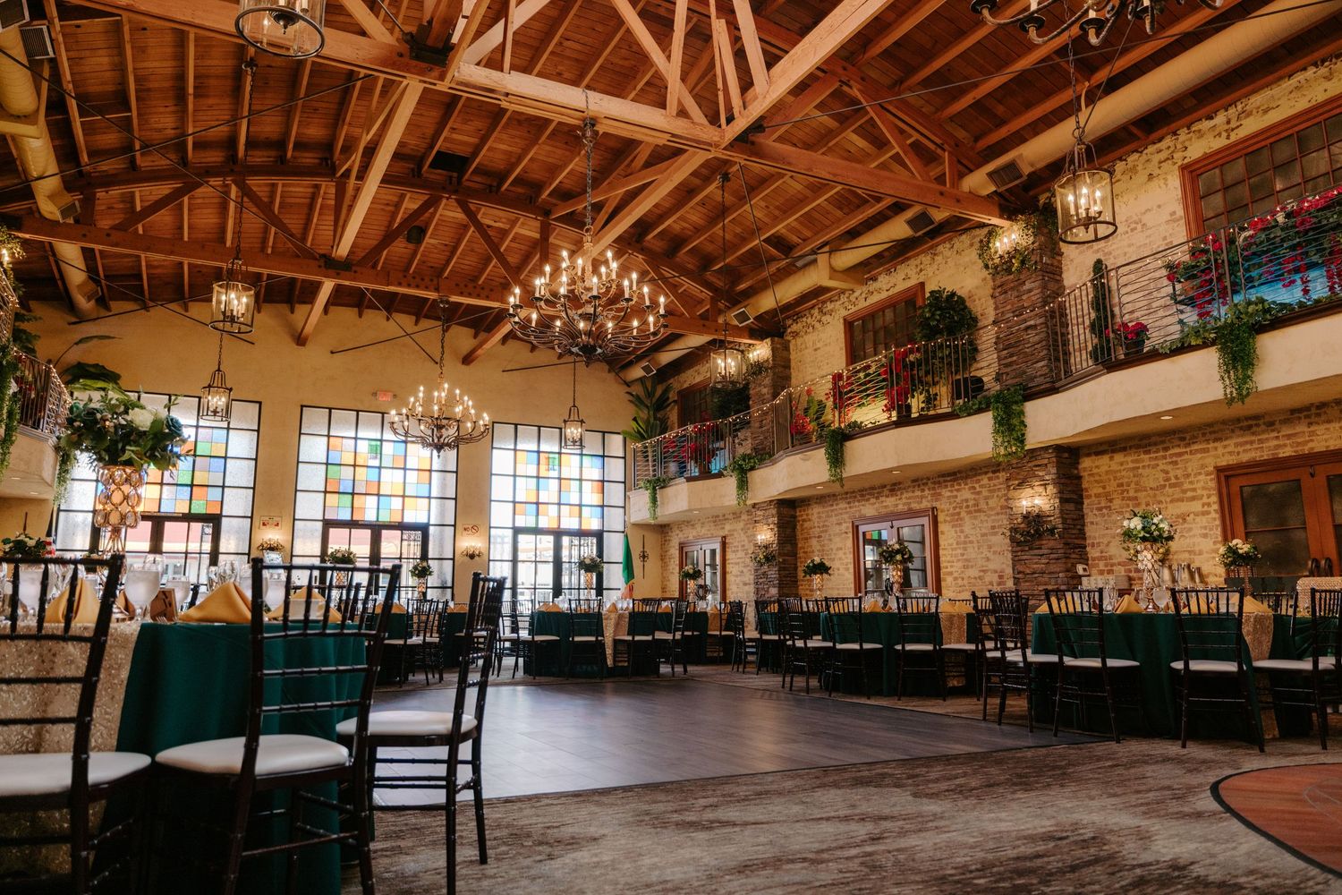 Interior panoramic view of a rustic wooden event venue with exposed beams, chandeliers and large windows.