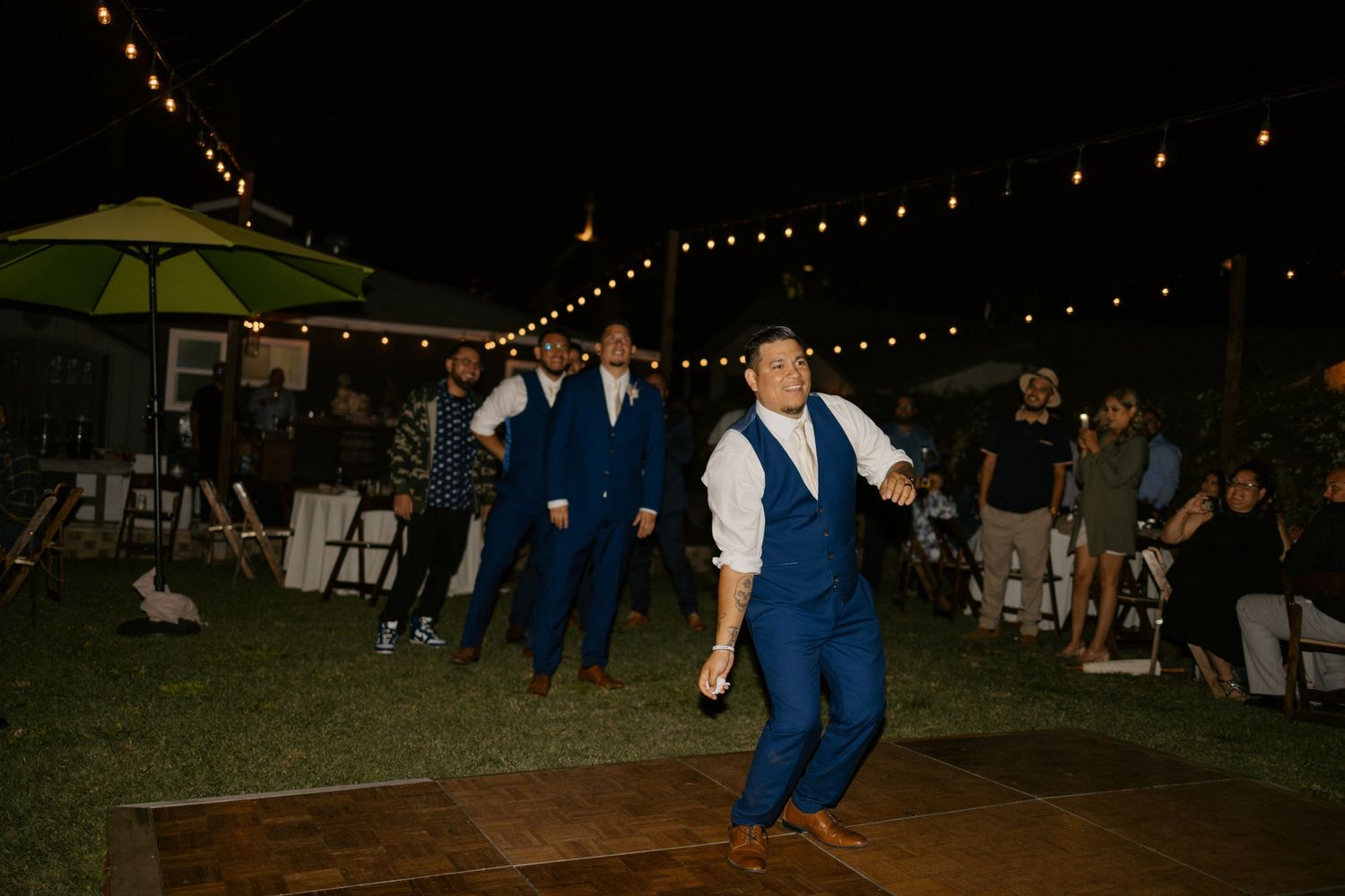 People dance enthusiastically on an outdoor dance floor during a nighttime wedding reception.