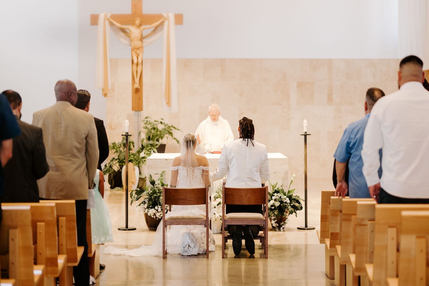 A wedding ceremony in progress at a church with white walls and crucifix.