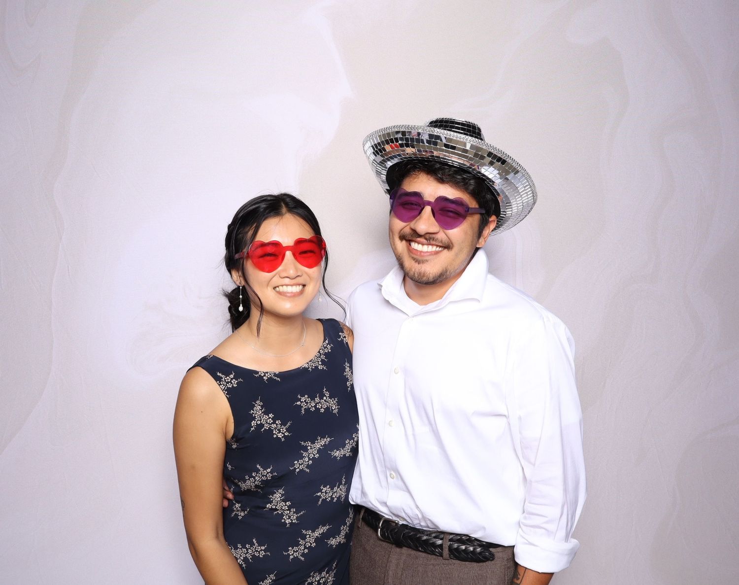 Two friends pose in a photo booth wearing oversized fun glasses and a sparkly sombrero hat at a party.
