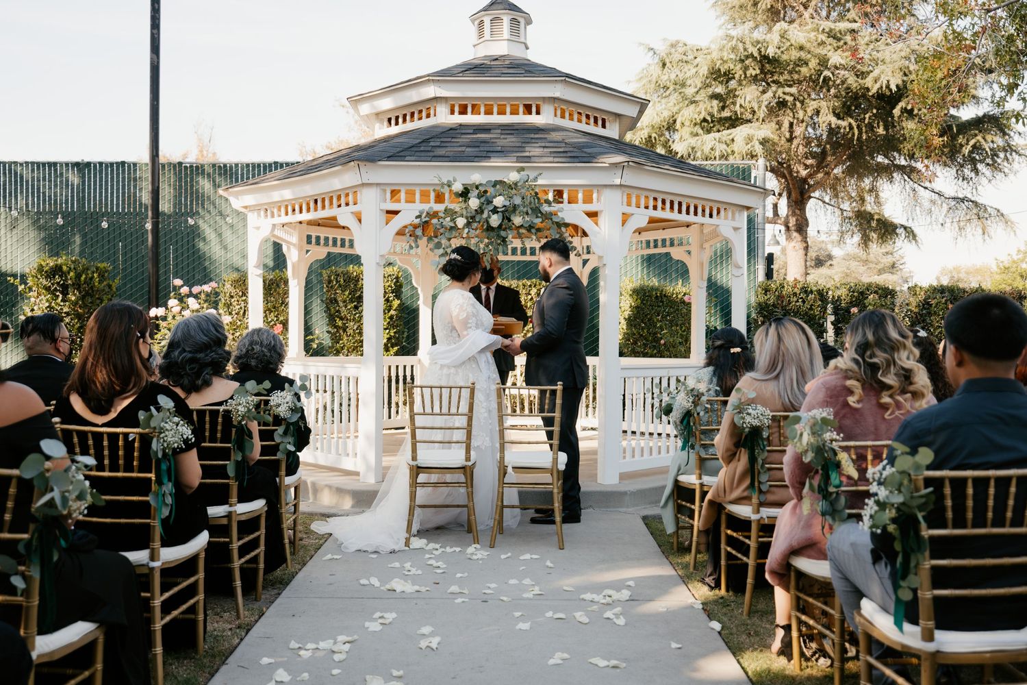 White gazebo and chairs set up for outdoor wedding ceremony with Mediterranean architectural details.
