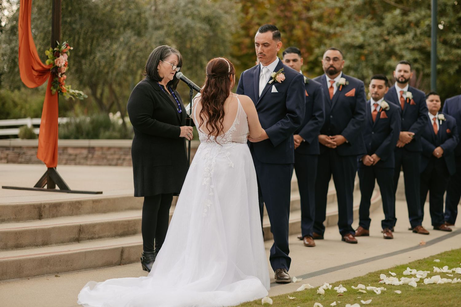 An outdoor wedding ceremony on stone steps with scattered flower petals.