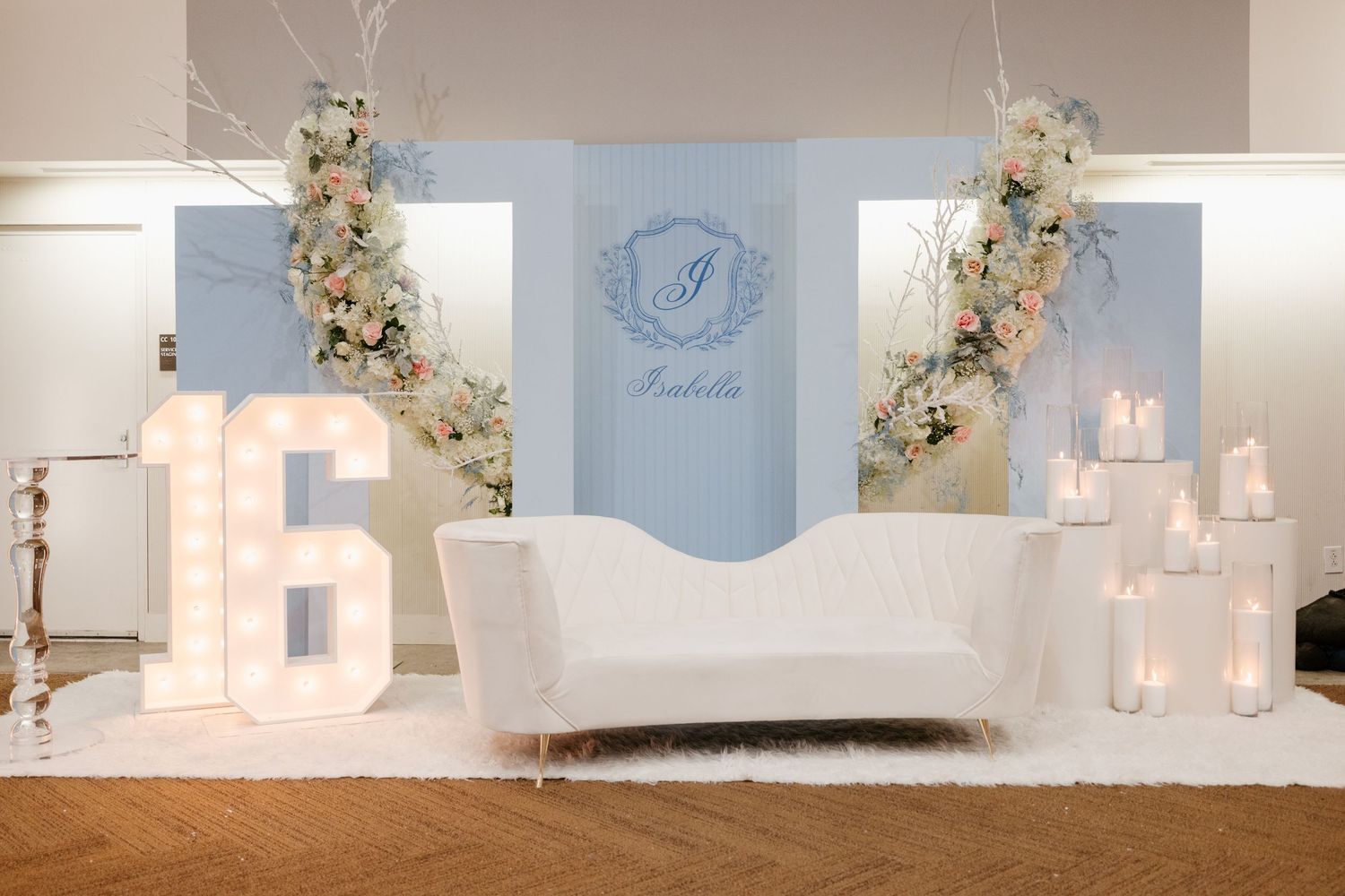 Elegant white lounge setup with light-up letters, floral arrangements and soft blue backdrop for special event.