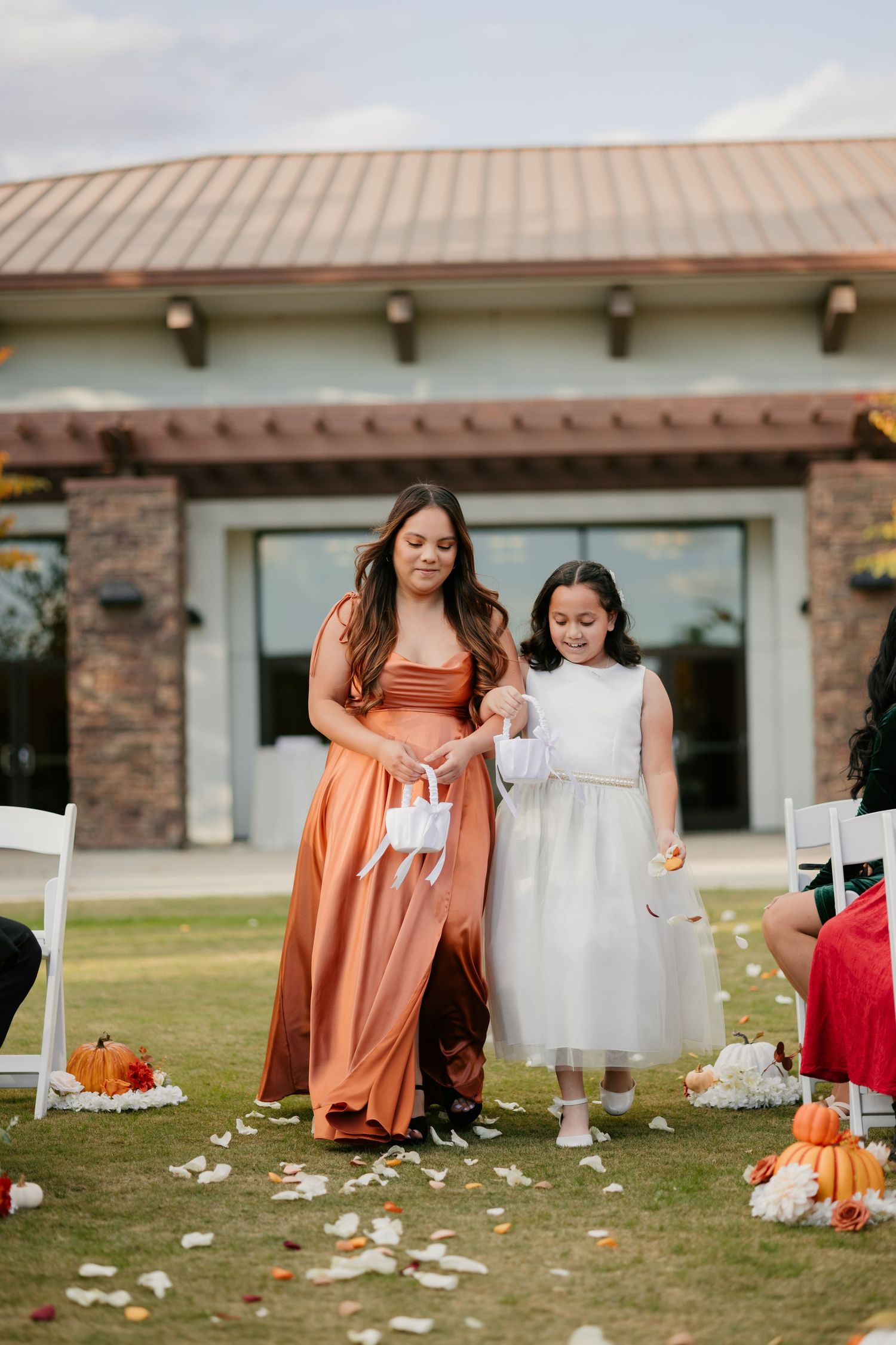 Two attendants walk down an aisle decorated with fall pumpkins and scattered petals.