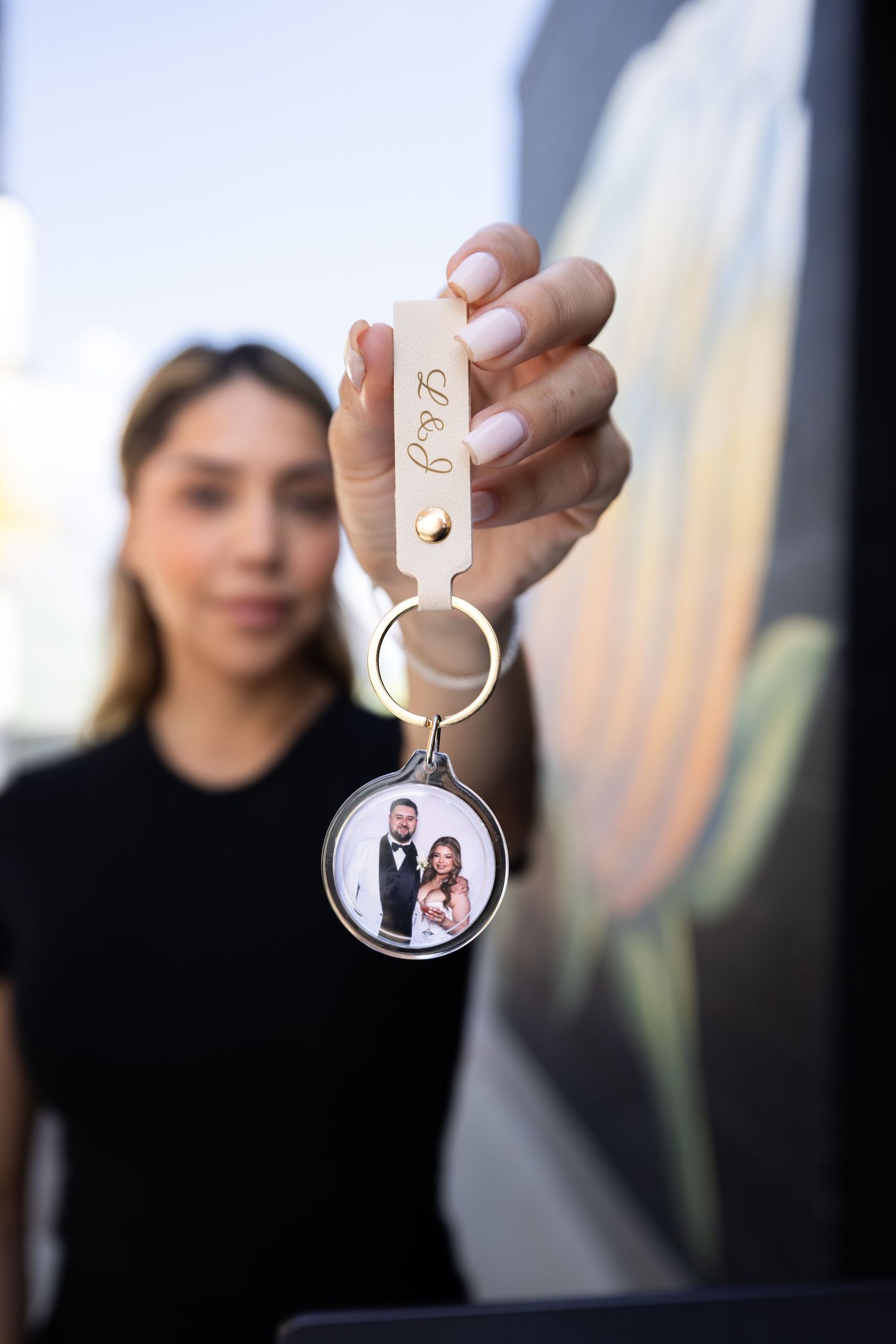 Woman holding a custom photo keychain with a couple's portrait and personalized leather tag.