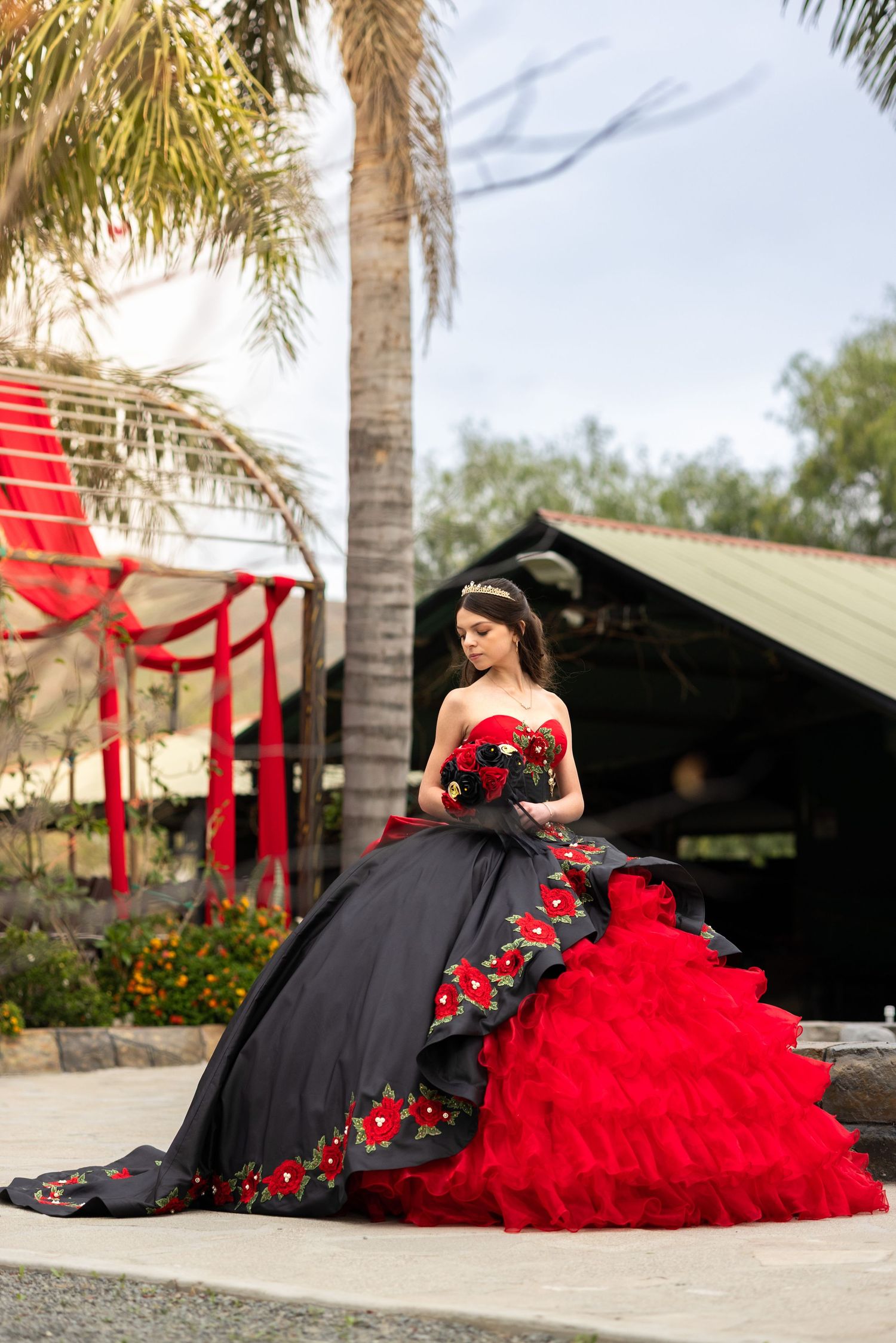Dramatic black and red quinceañera dress with floral details photographed by palm trees.
