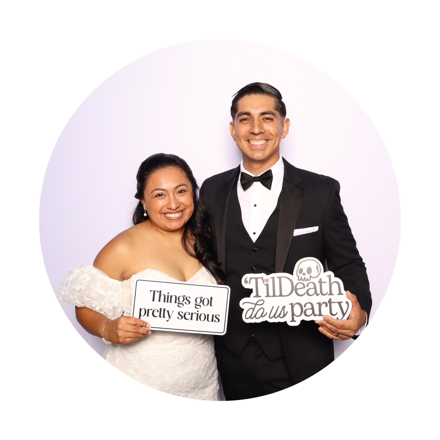 Newlywed couple in wedding attire posing in photo booth holding fun signs at wedding reception.