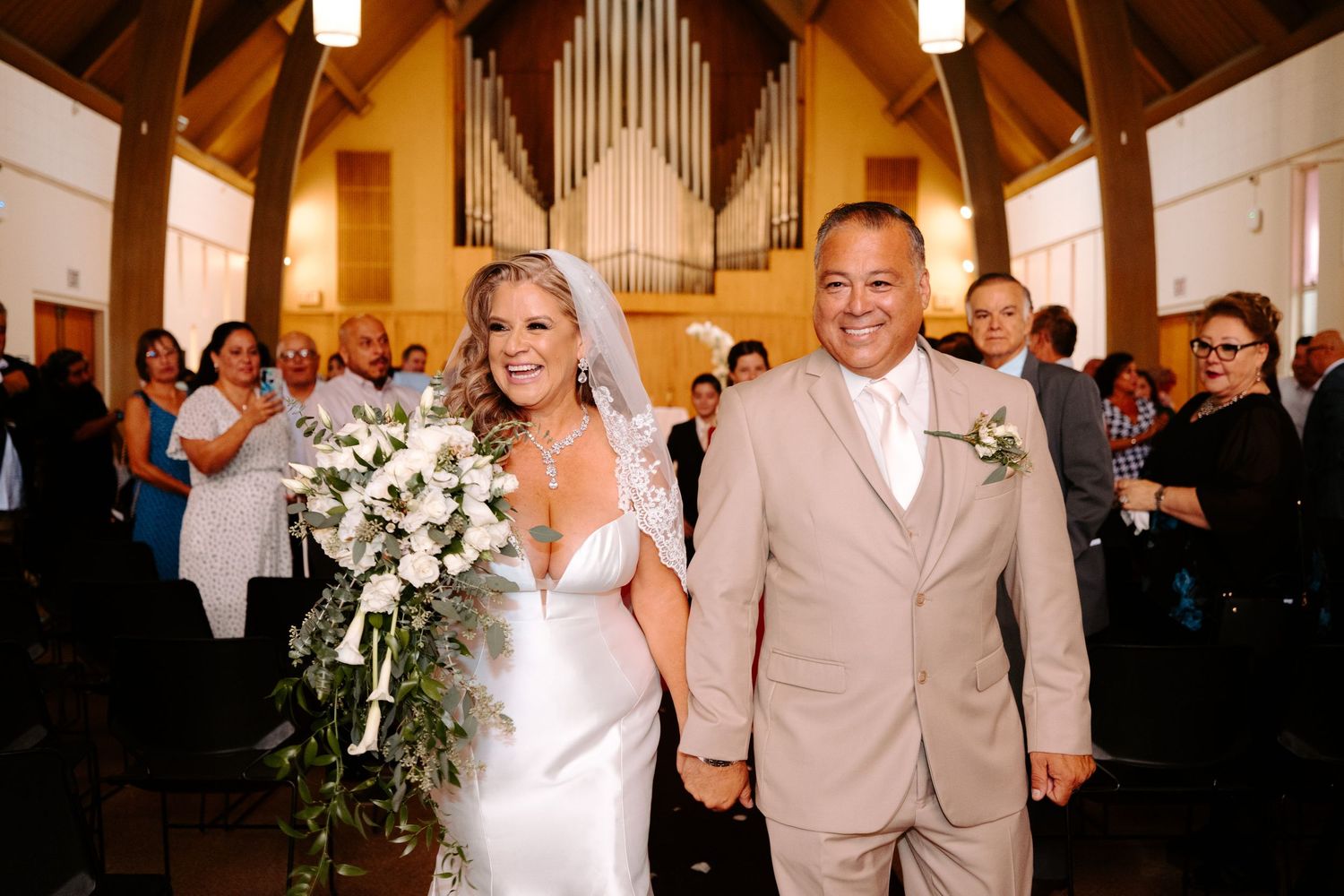 Couple walks down church aisle after ceremony with guests applauding in background.