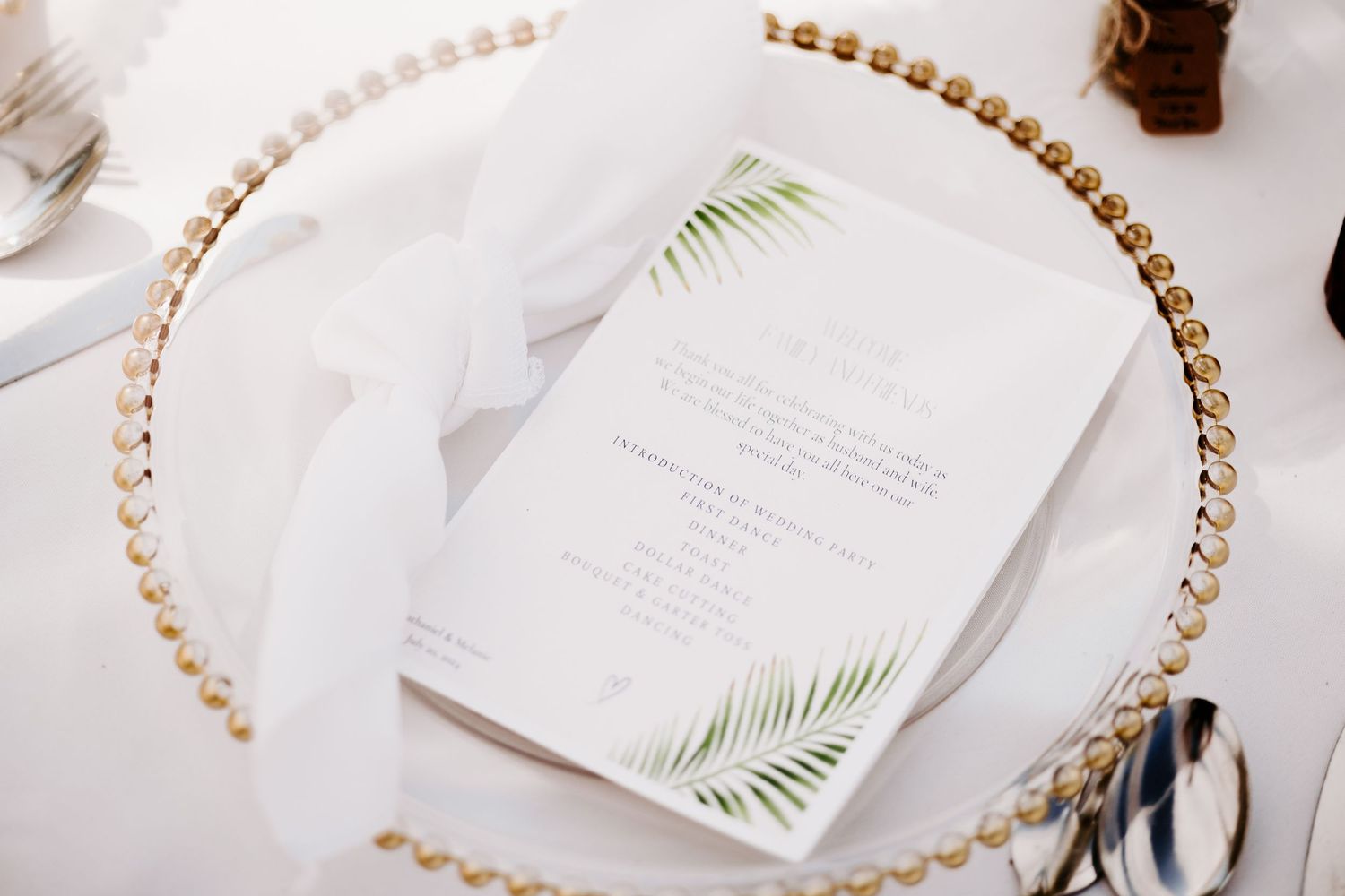 Wedding menu card with palm leaf design on gold-rimmed charger plate.