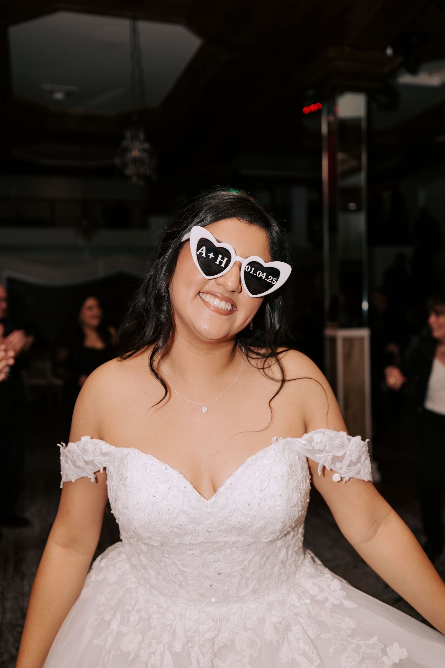 A bride wearing heart-shaped sunglasses and white dress celebrates at reception.