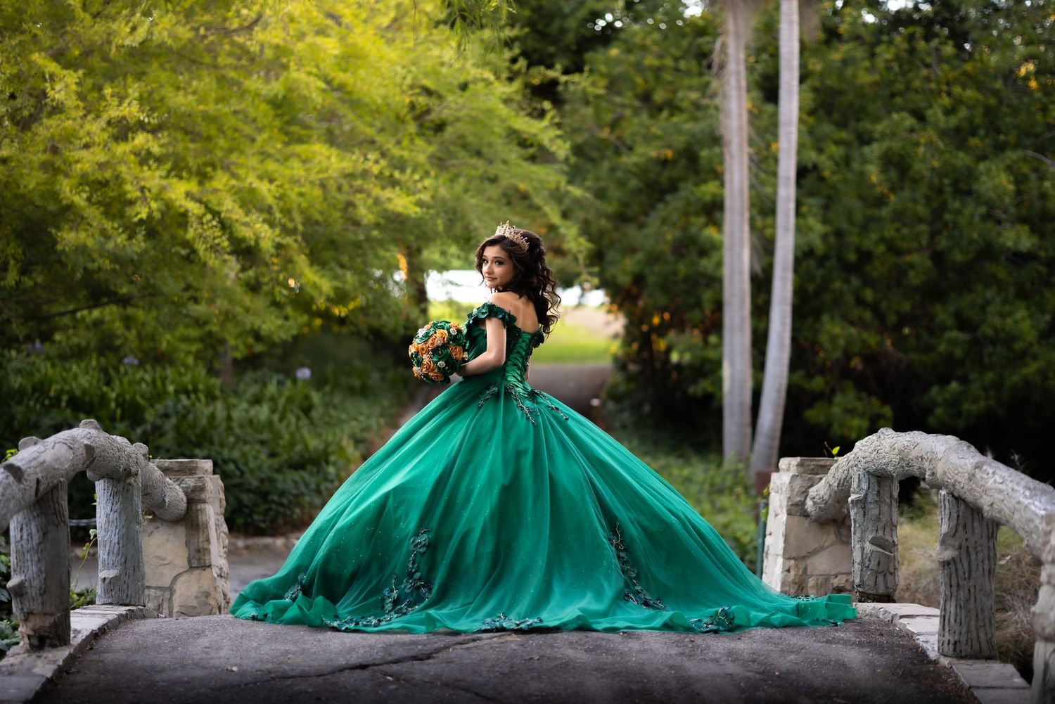 Dramatic emerald ball gown photographed in series against a backdrop of tall trees at sunset.