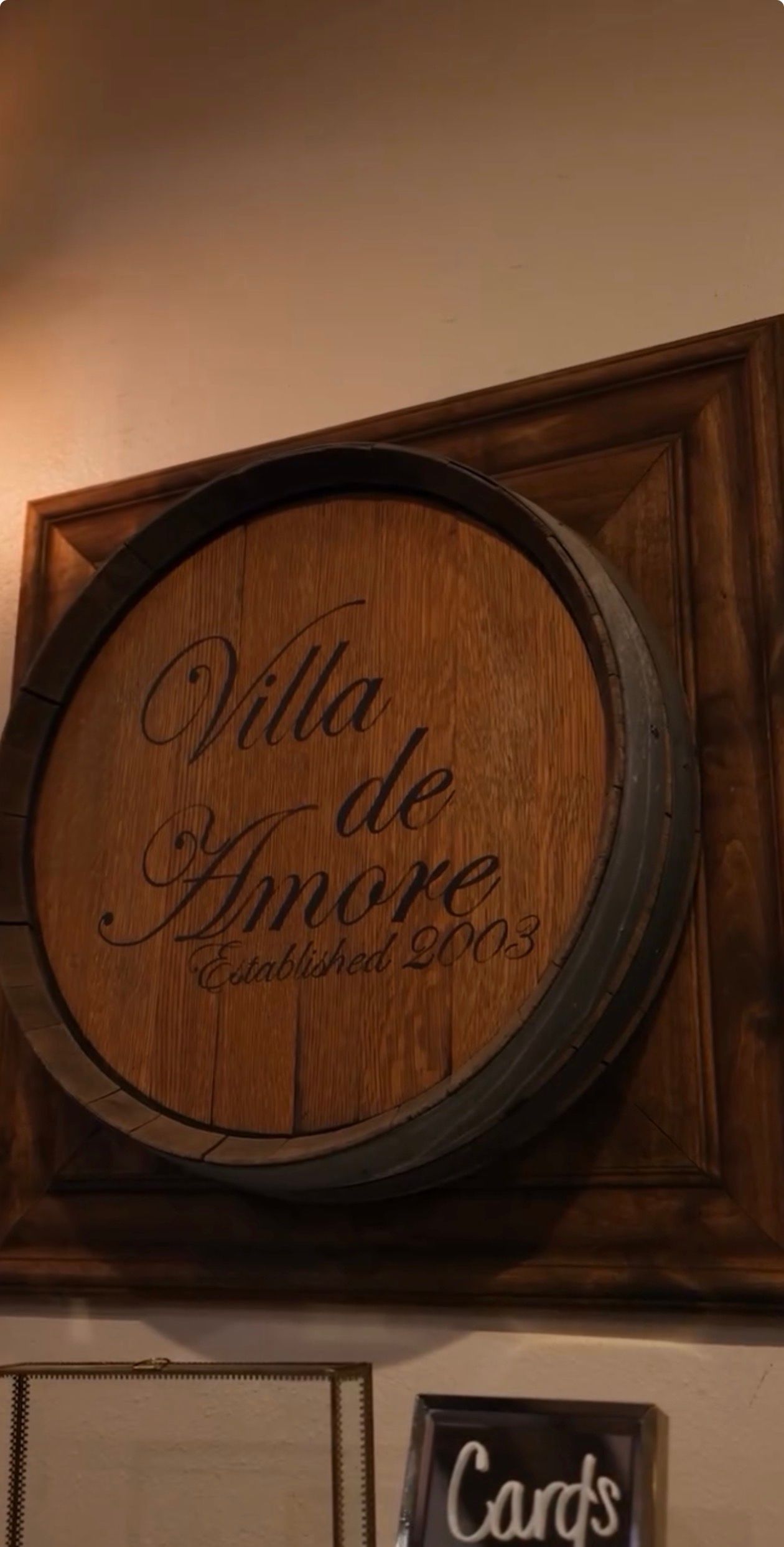 Wooden wine barrel signs with elegant script text displaying 'Villa Amore' mounted on a brown wall above a 'Cards' sign.