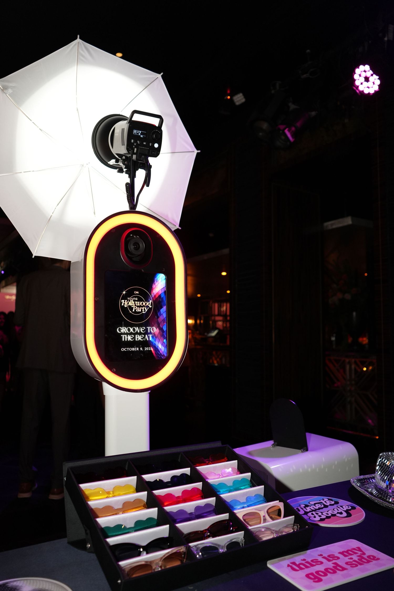 Professional photography lighting setup with white umbrellas and ring lights illuminating colorful display boxes.