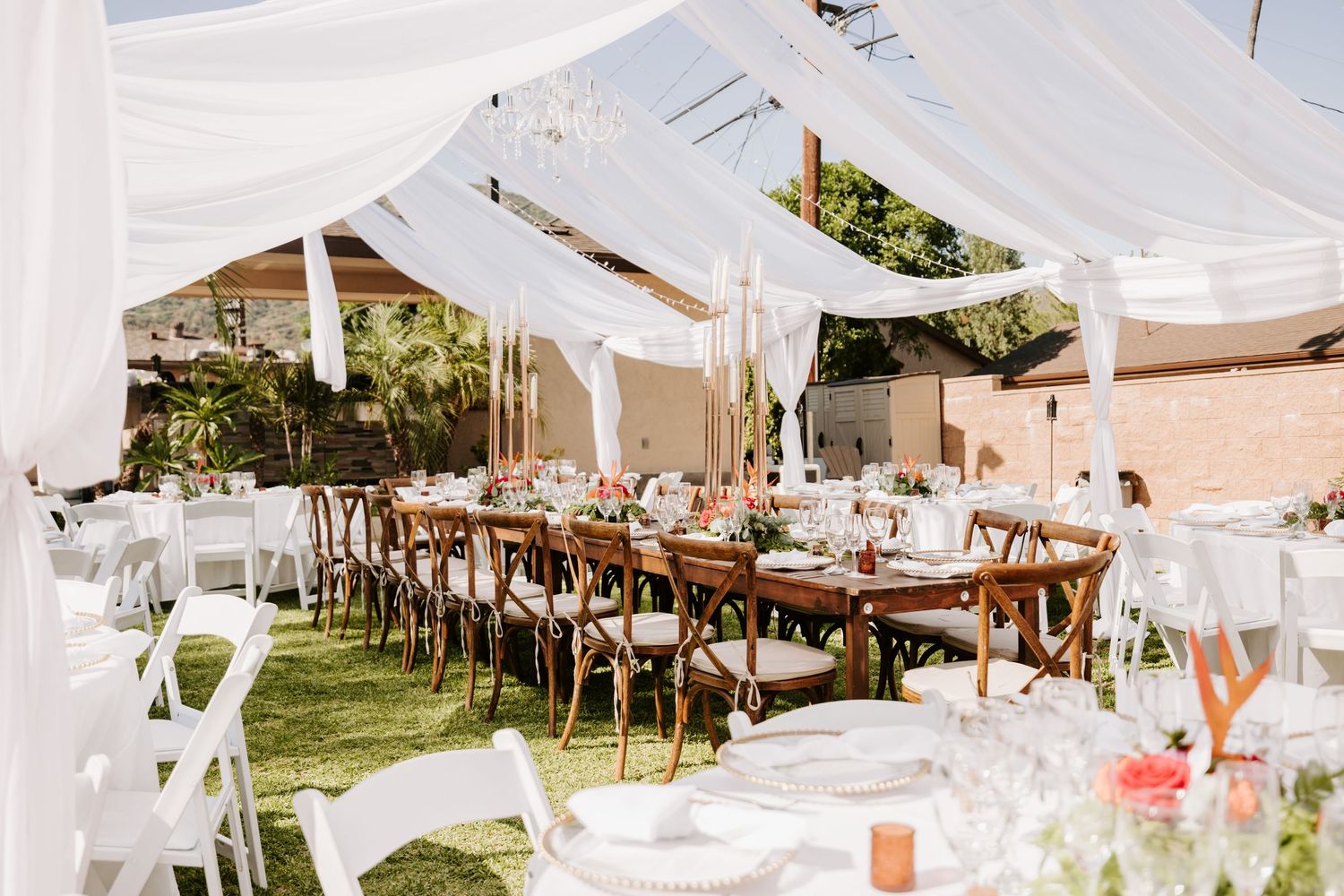 Outdoor wedding reception setup with white tent draping and wooden farm tables.