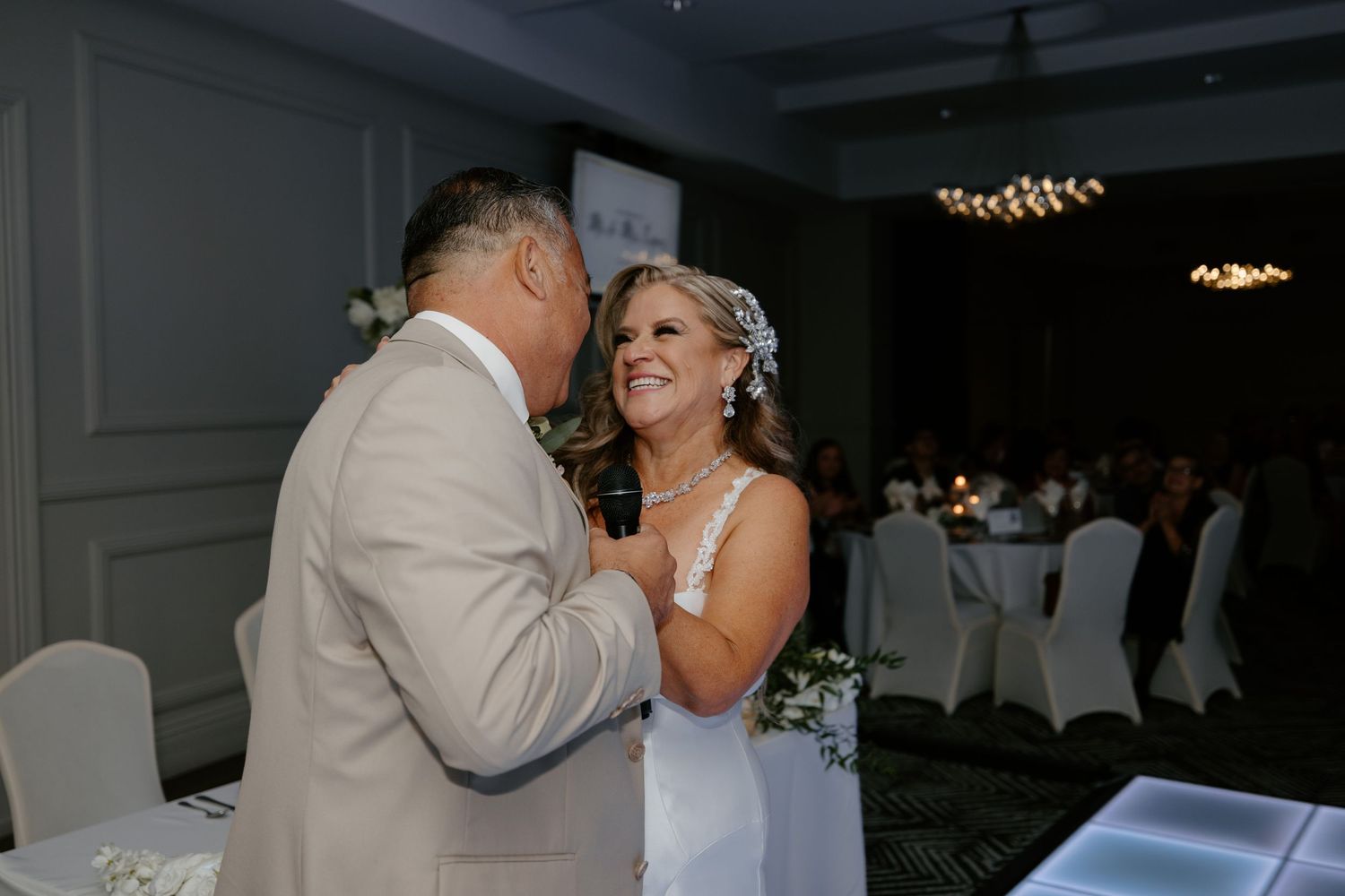 Wedding reception dance in an elegantly lit ballroom with guests looking on.