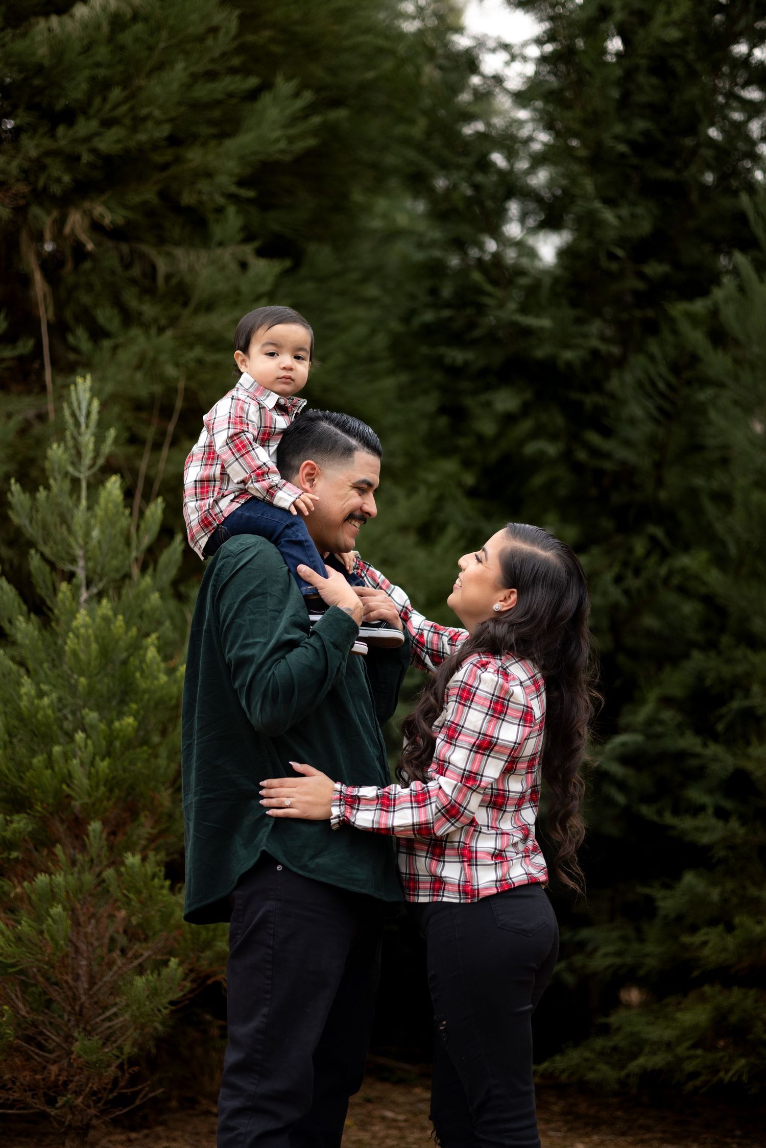 Family sharing playful moments during outdoor portrait session among pine trees.