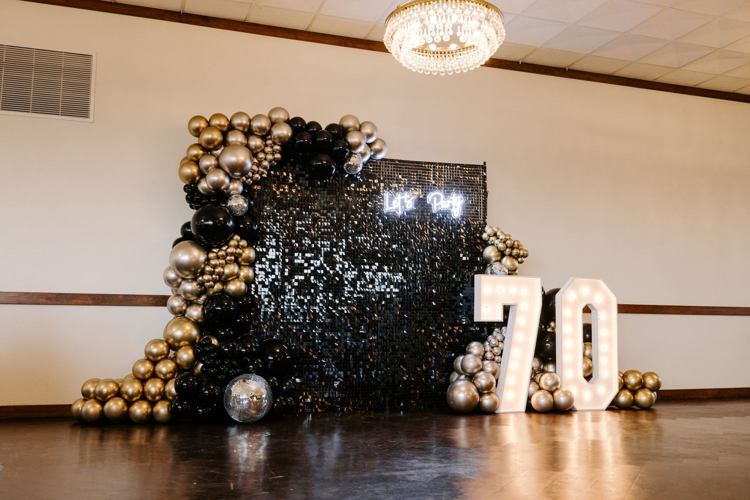 Modern party backdrop with black and gold balloon arch and illuminated number display.