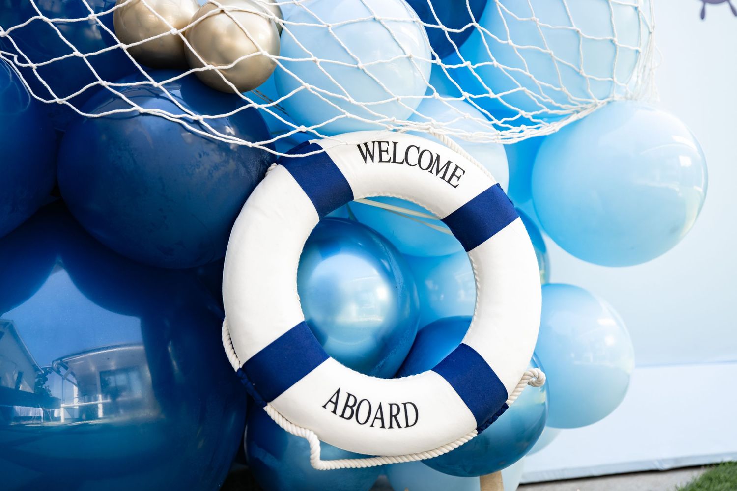 A nautical themed life preserver decoration with 'Welcome Aboard' text surrounded by blue balloons.
