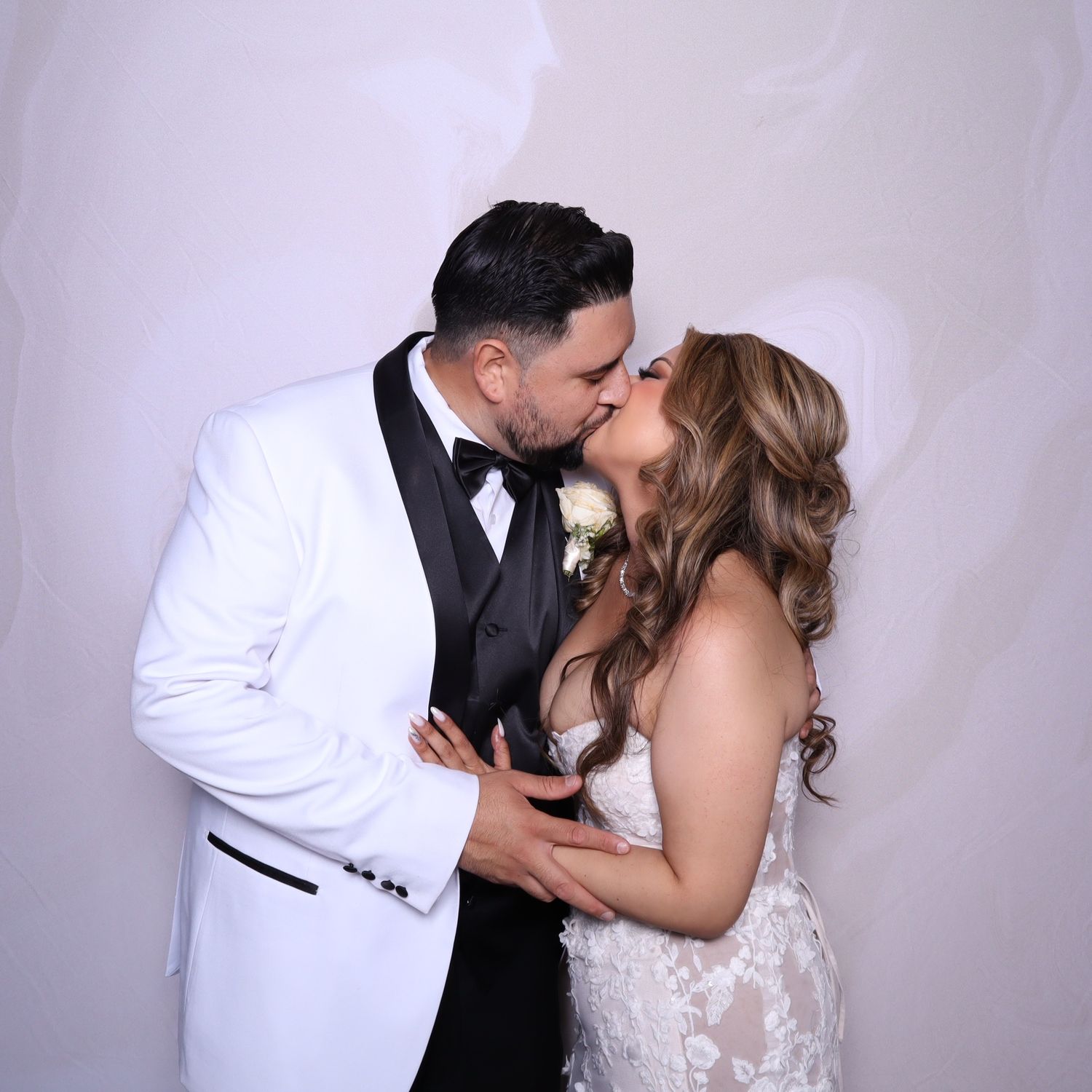 A bride and groom share a romantic kiss, dressed in wedding attire against a white backdrop.