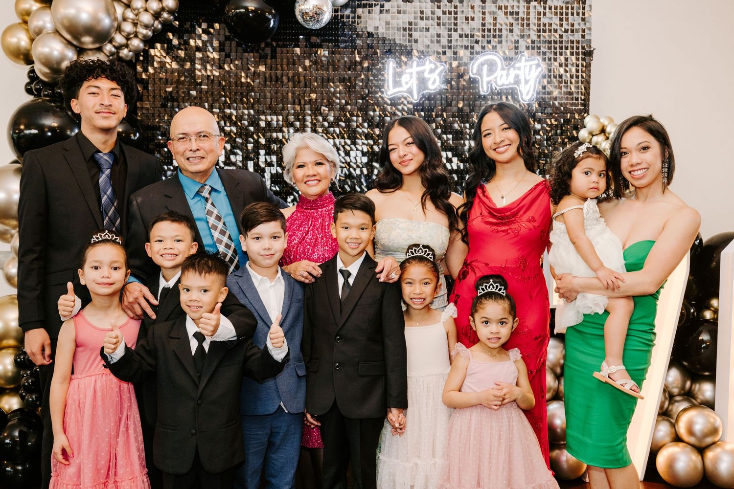 Large group celebrates at a formal event with sparkly decorations and festive attire.