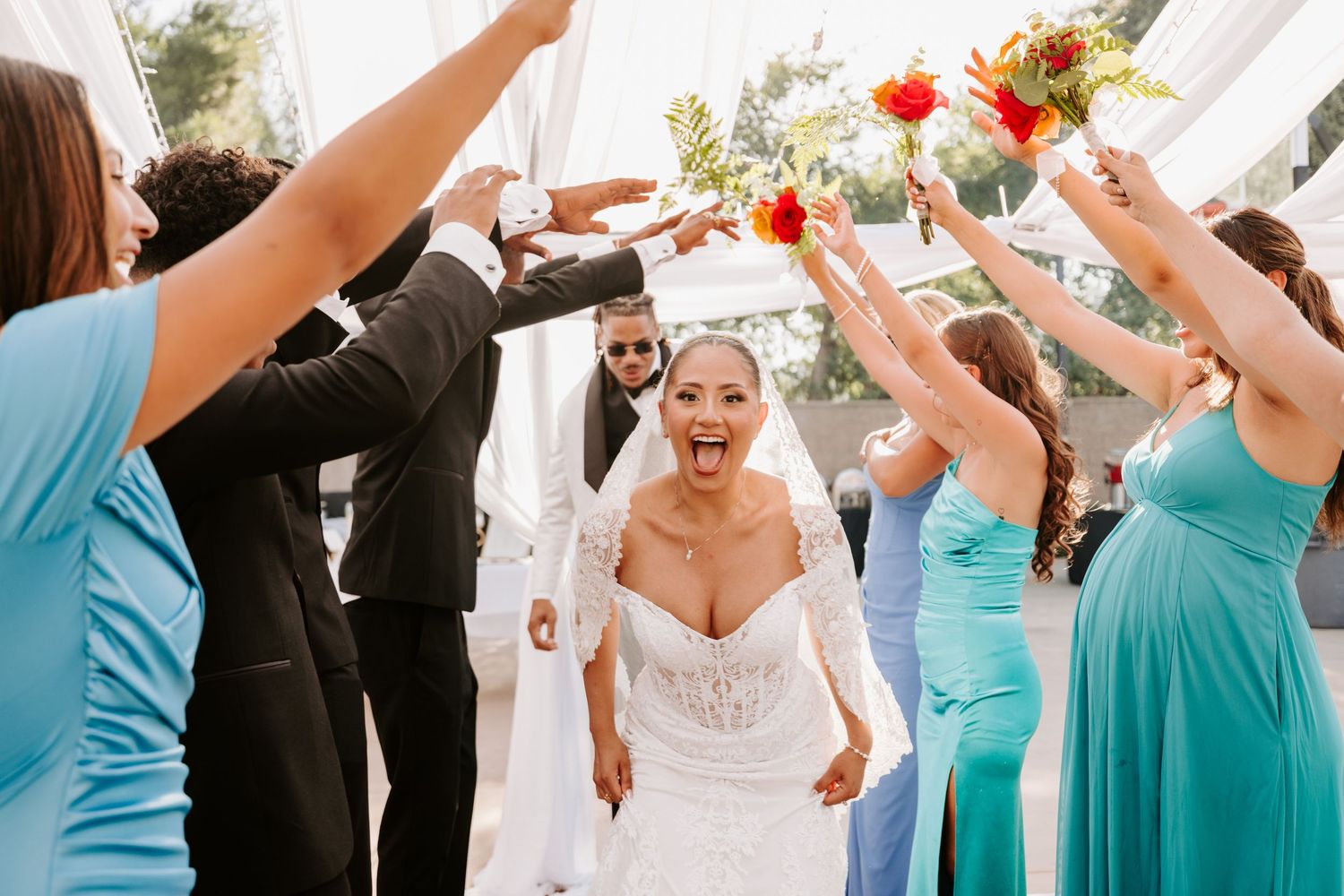 Wedding celebration under white tent with bridal party raising hands in celebration.