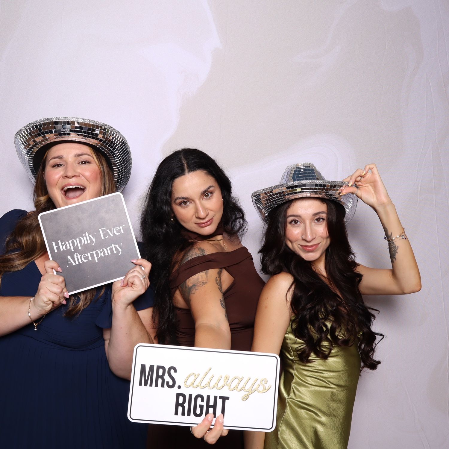 Three women posing in a photo booth with disco hats and signs reading Happily Ever Afterparty and Mrs. Always Right.