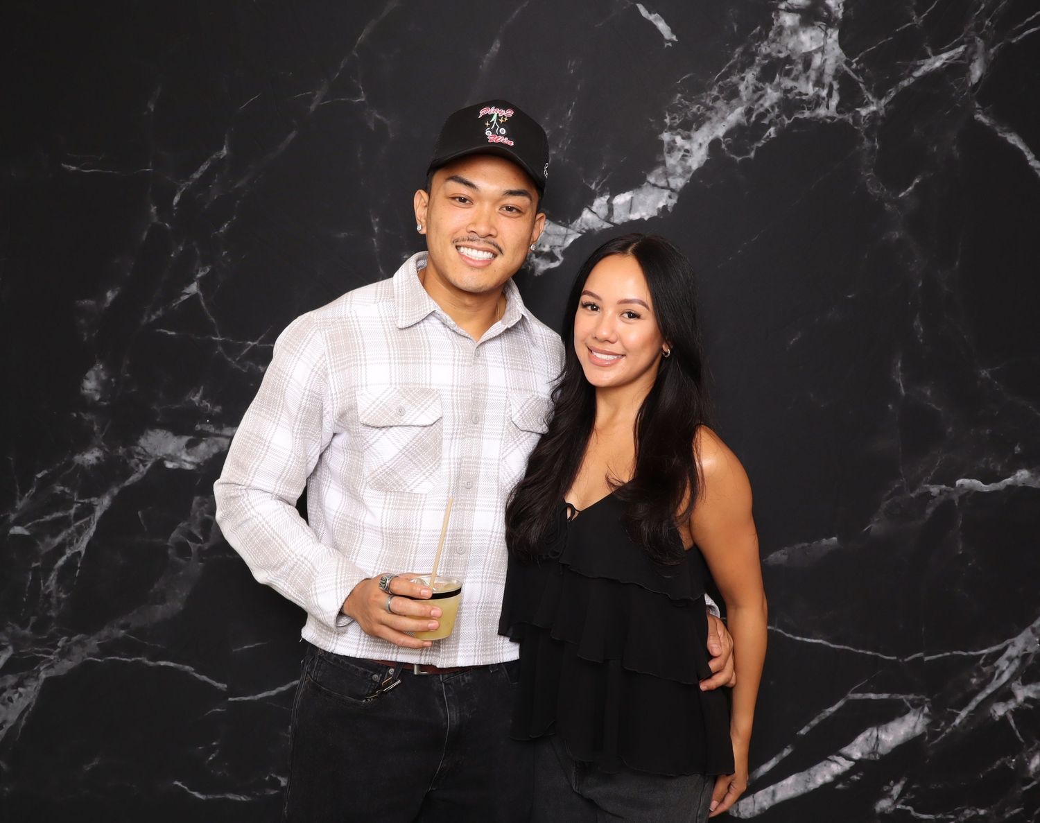 A young couple smiles together in front of a dark marble backdrop at a social event.