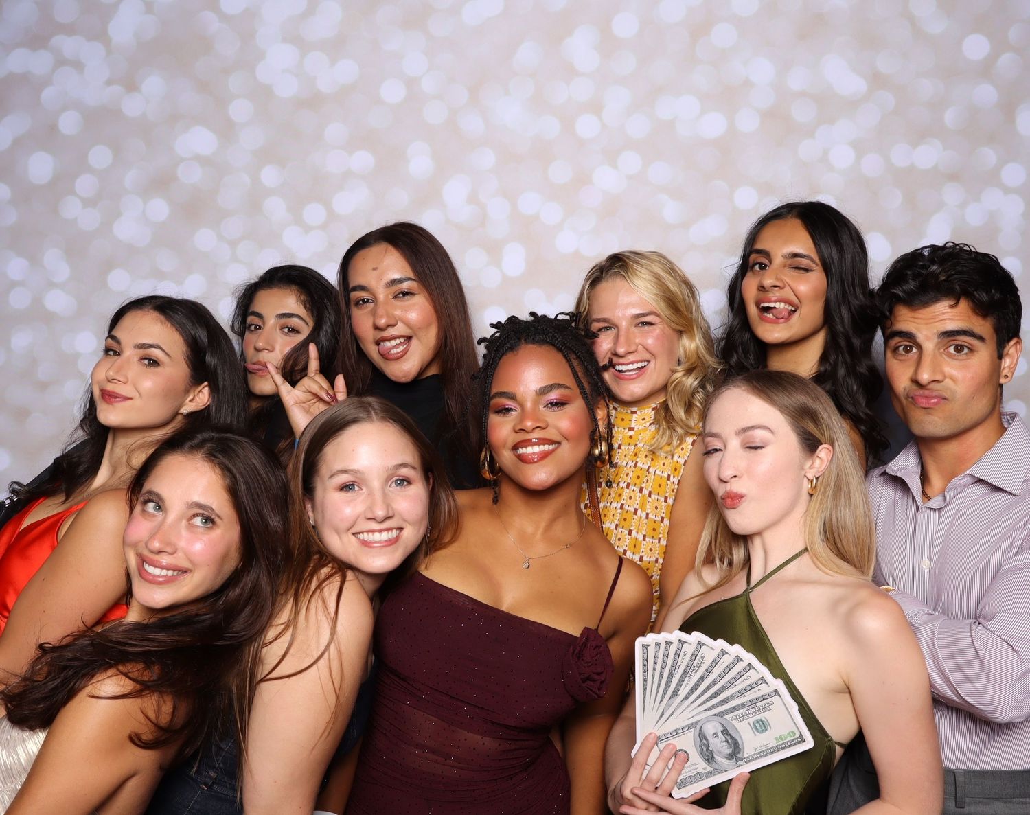 A group of friends laughing and smiling together at a social gathering with festive lighting in the background.