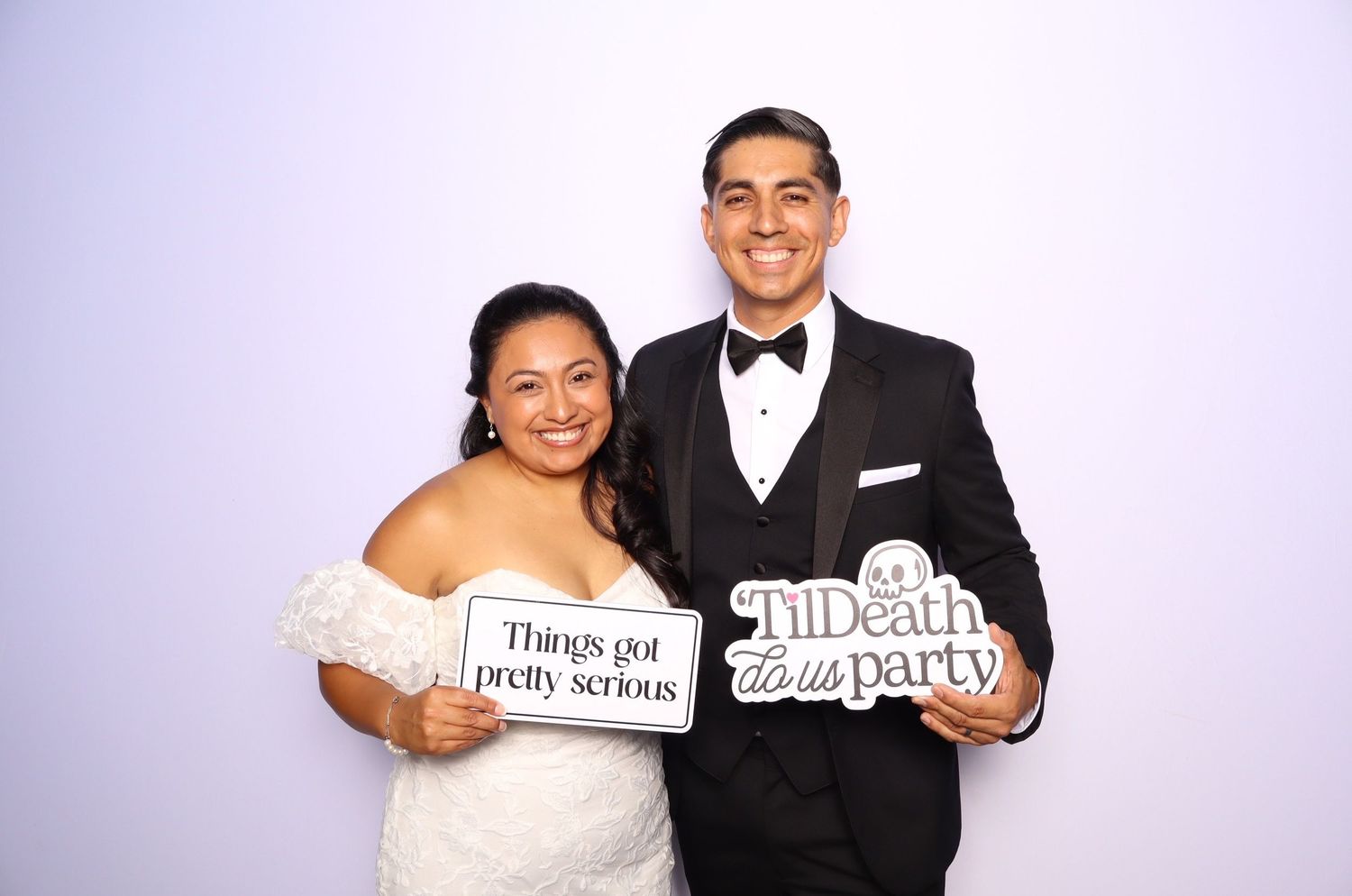 Wedding couple holds fun photo booth props and signs while posing together in formal attire.