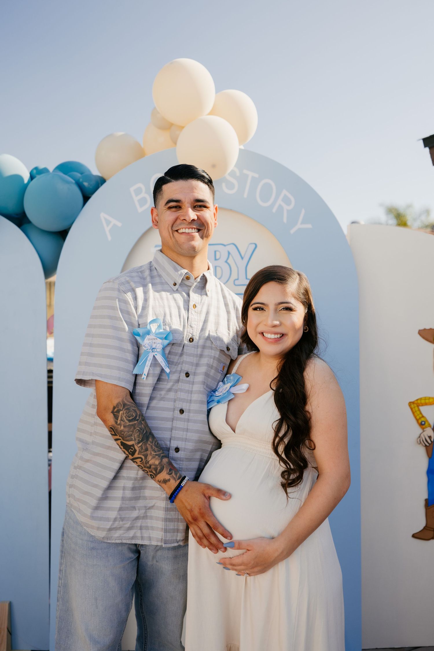 Expectant couple poses at baby shower with blue and white balloon arch backdrop.