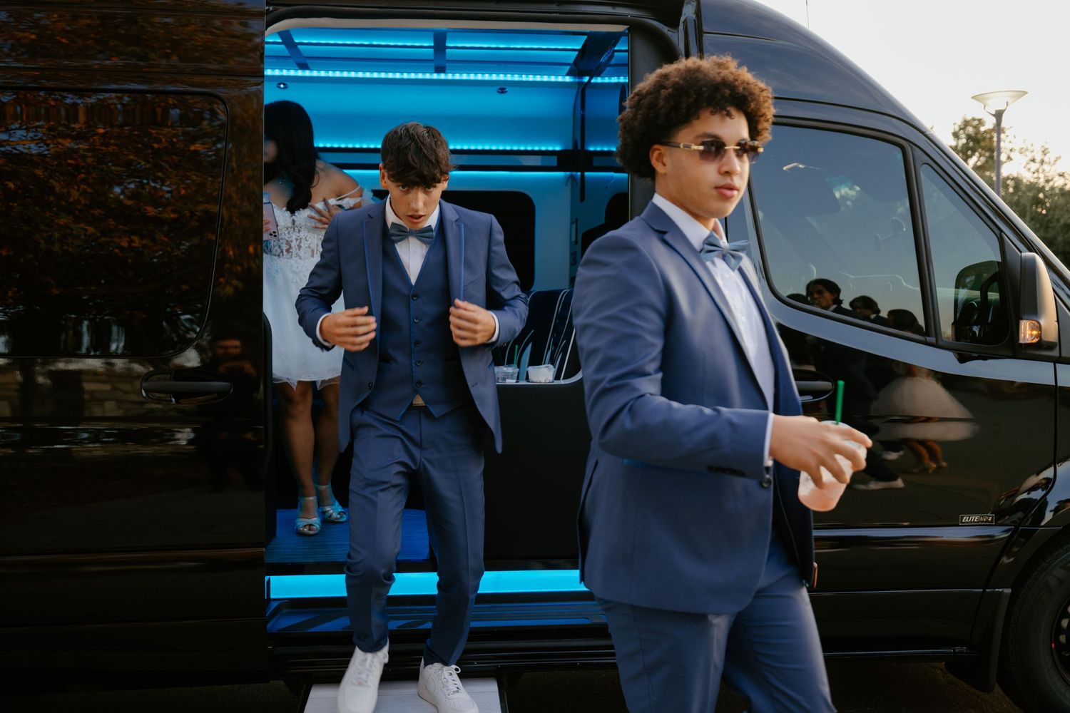 Two men in navy blue suits standing by a blue van checking their phones.