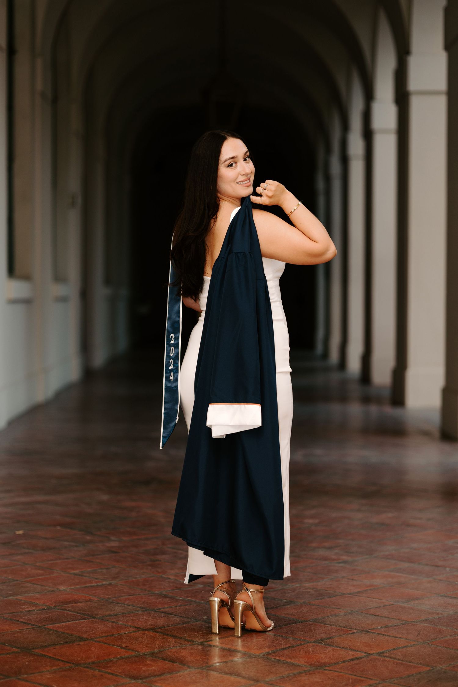 A person poses in a black and white contrasting maxi dress with brown sandals in an arched hallway.